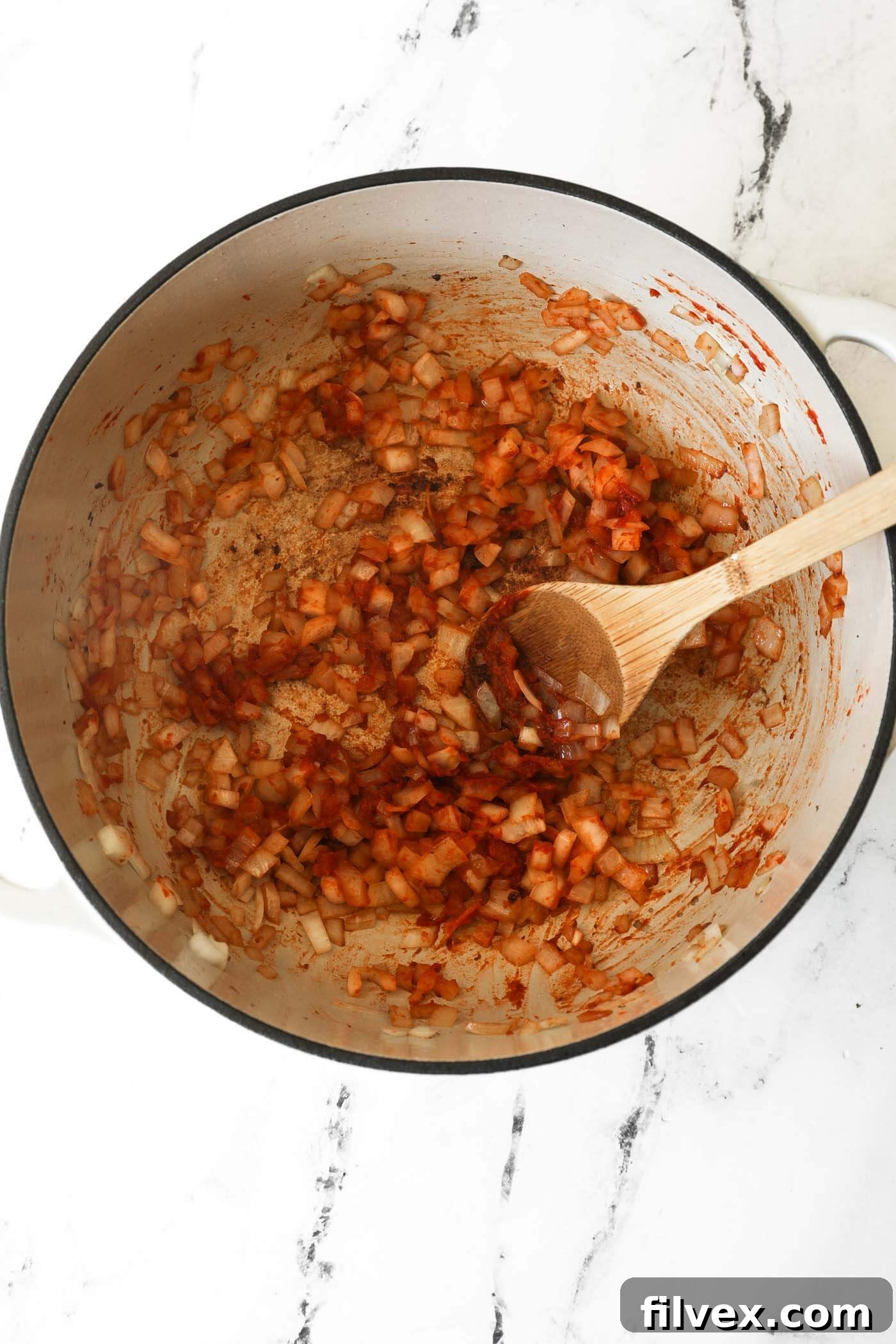 Adding tomato paste to the onions in the Dutch oven and stirring.