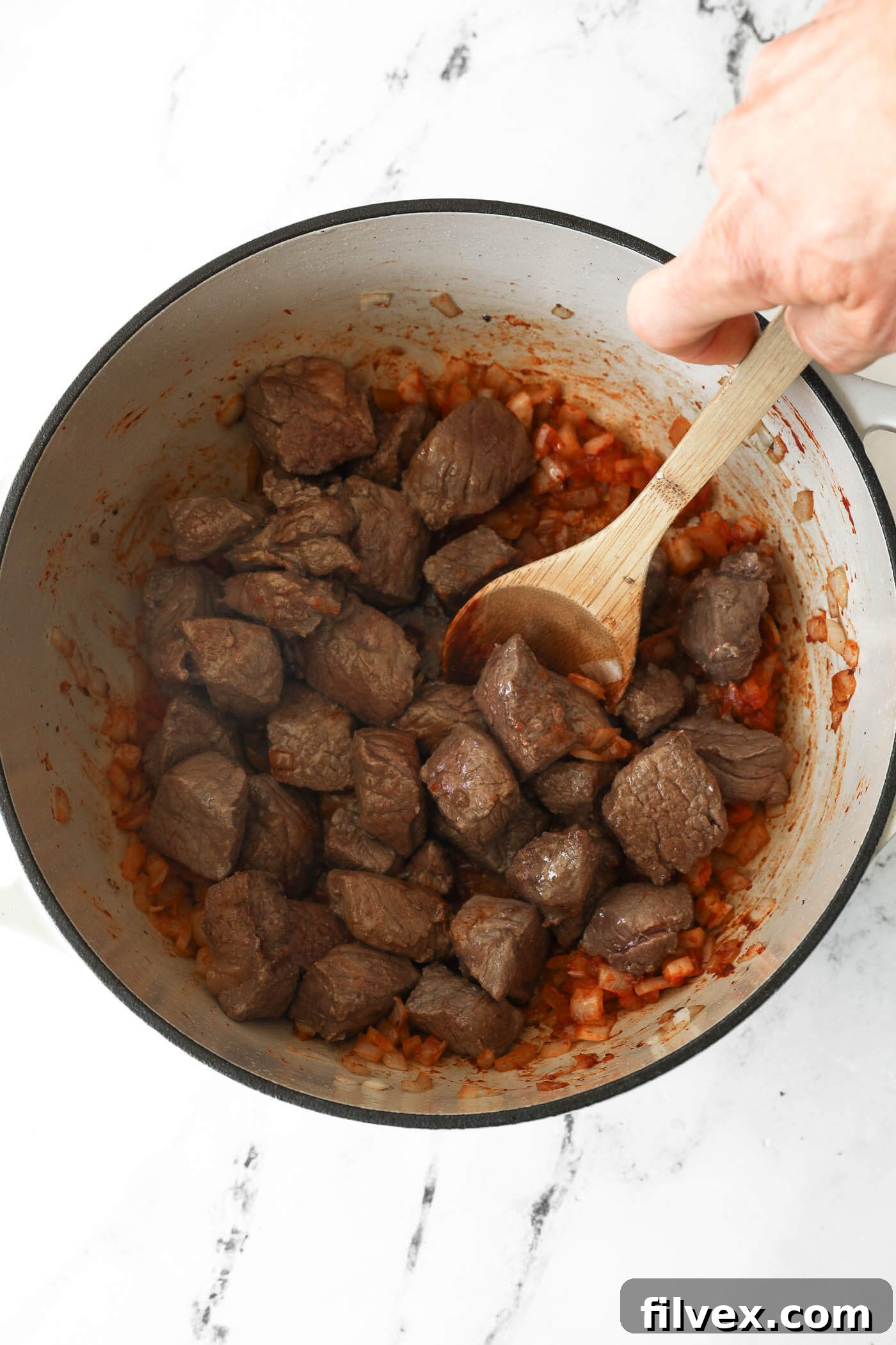 Adding the seared beef back into the Dutch oven with onions and tomato paste.