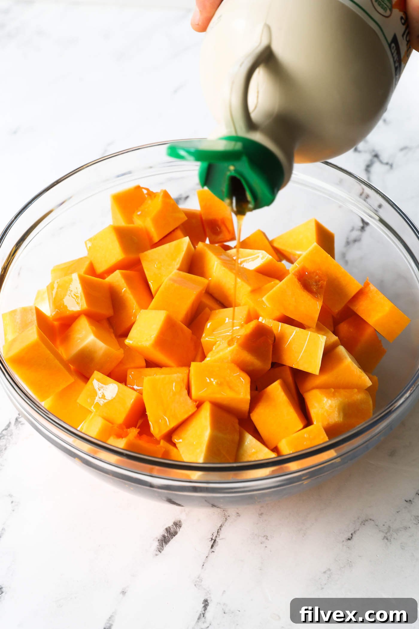 Pouring maple syrup over butternut squash cubes in a bowl.