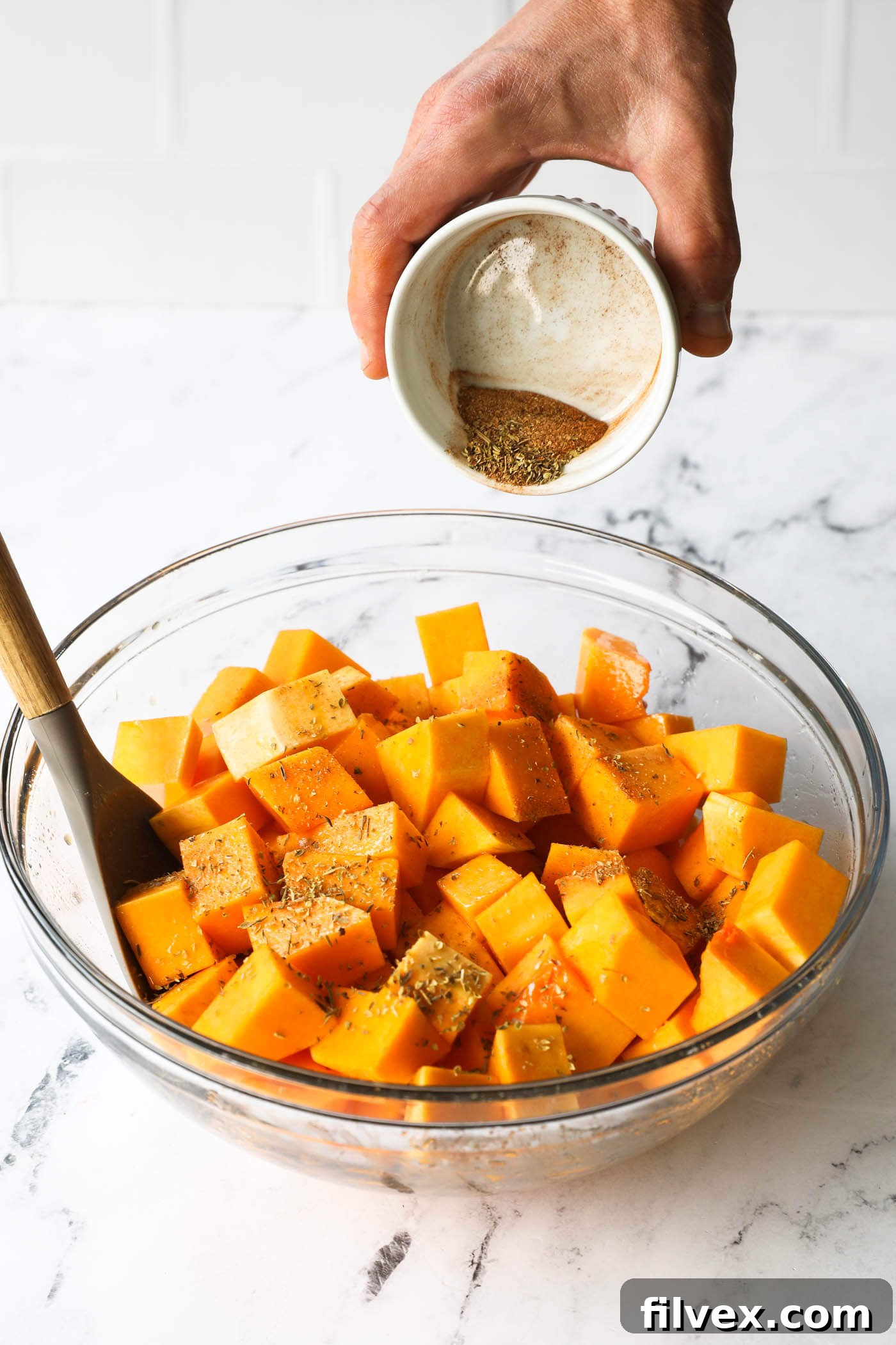 Tossing butternut squash cubes with seasoning blend in a bowl.