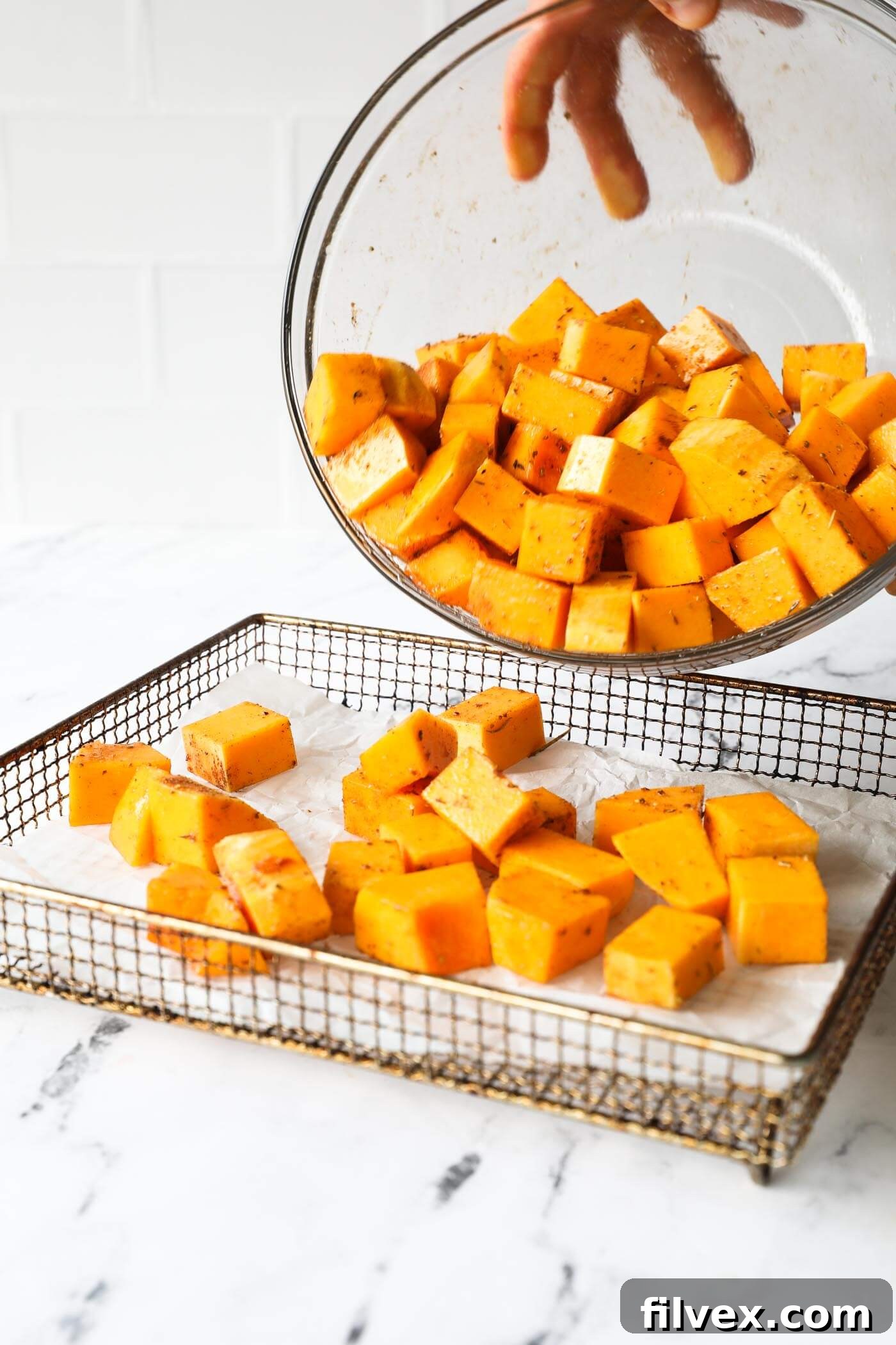 Spreading seasoned butternut squash cubes in a single layer in an air fryer basket.
