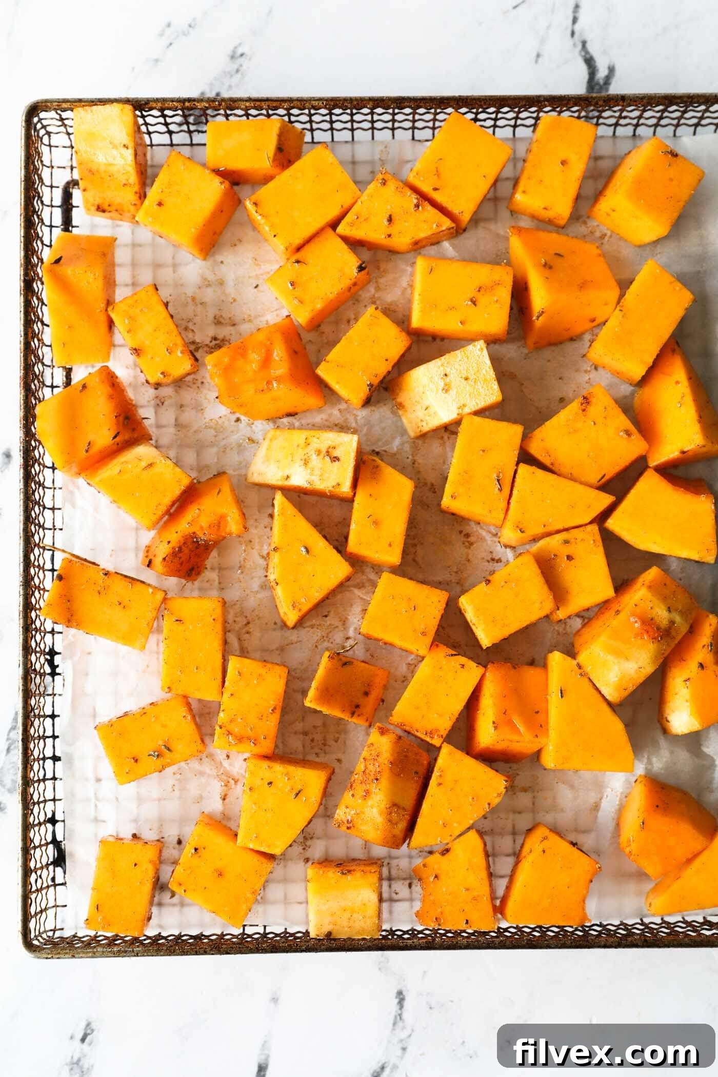 Air fryer basket with cooking butternut squash cubes inside.