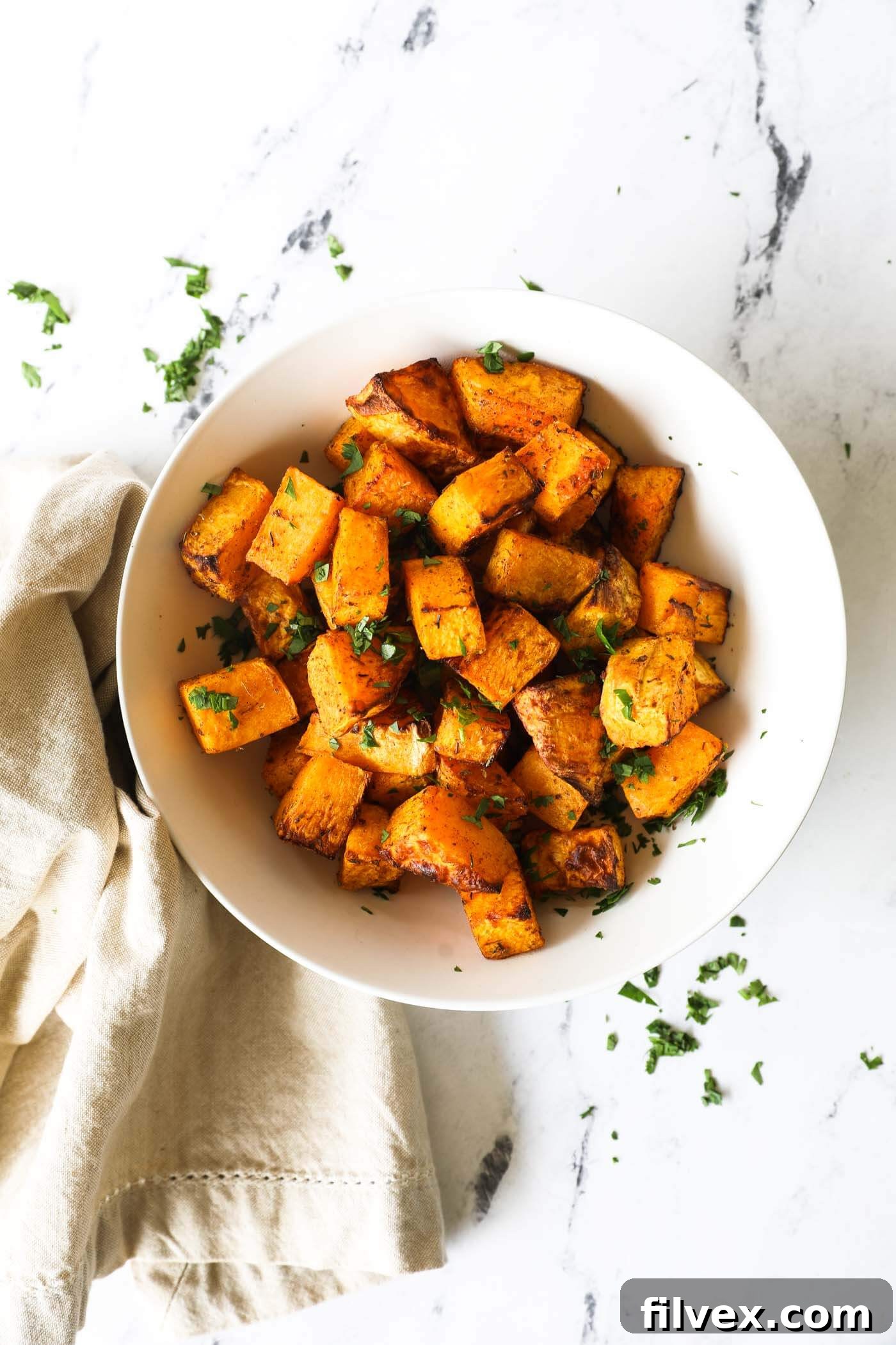 Close-up of perfectly cooked air fryer butternut squash cubes in a white bowl.