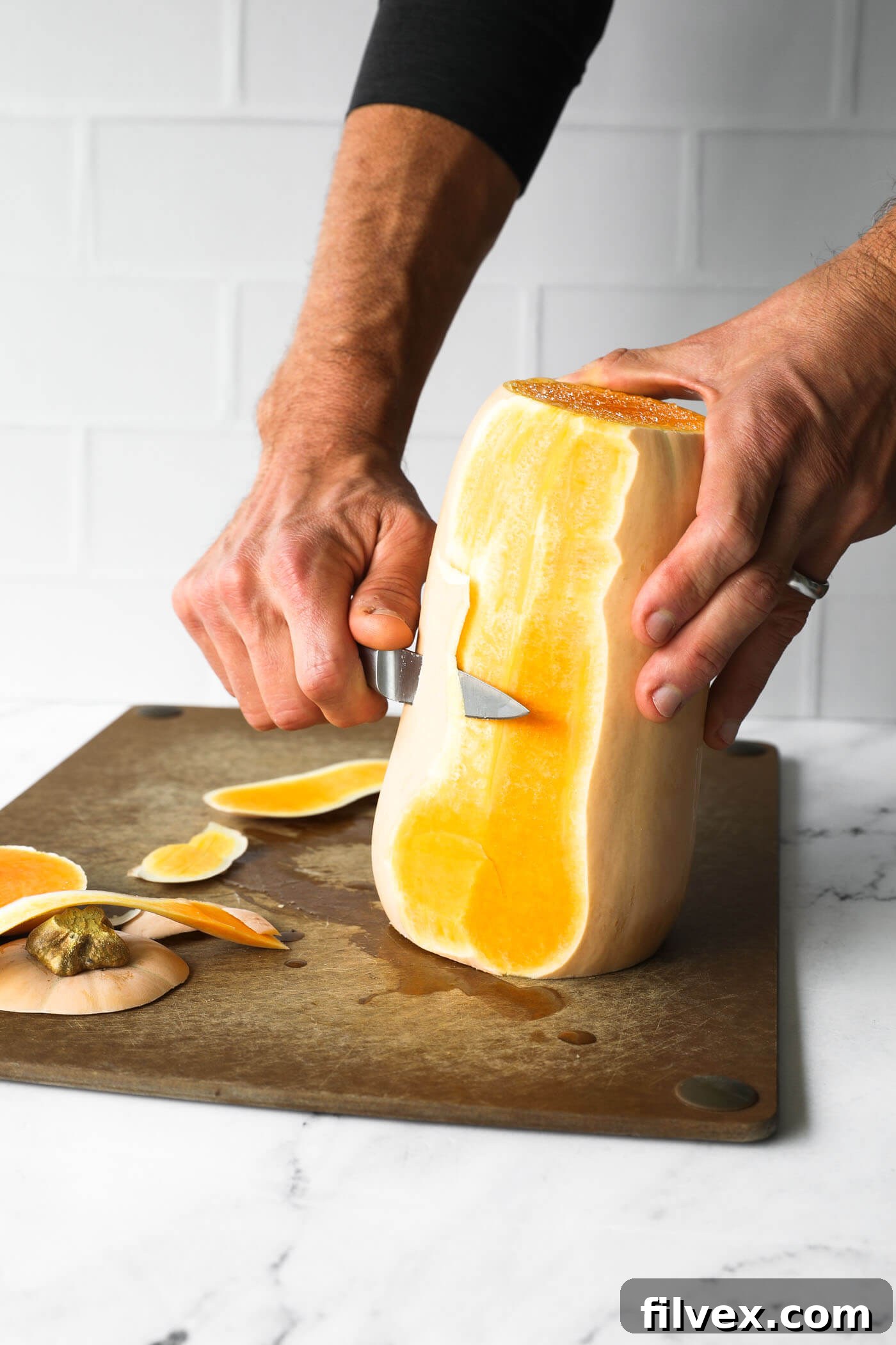 Peeling the skin off a butternut squash with a vegetable peeler.