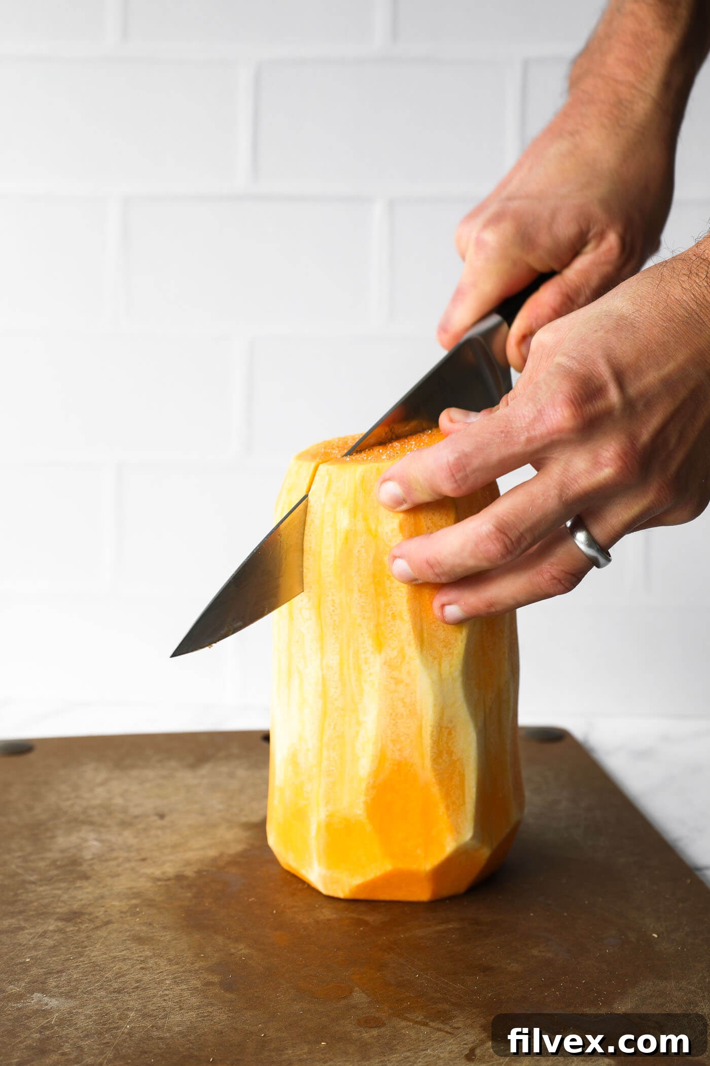 Slicing a peeled butternut squash in half lengthwise.