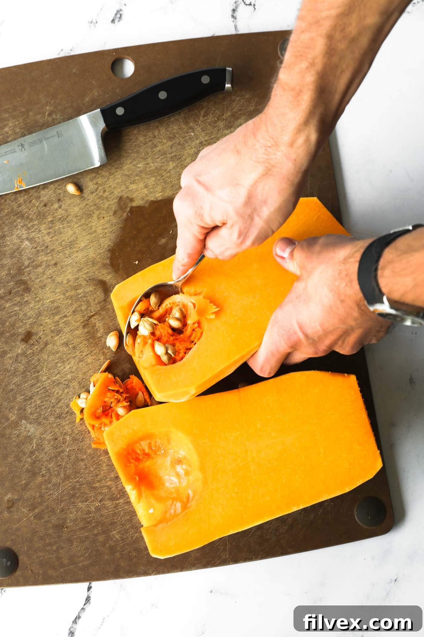 Scooping out seeds from a butternut squash half with a spoon.