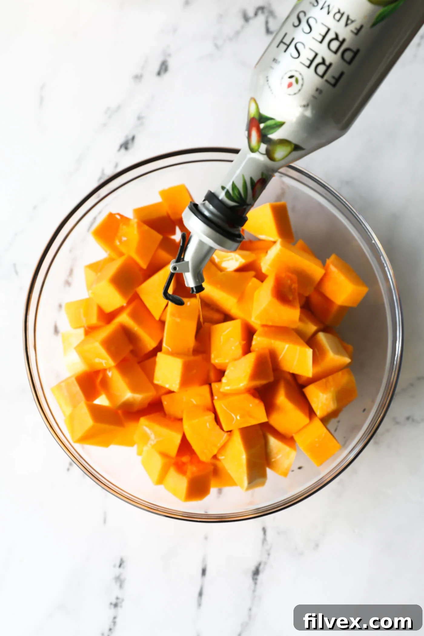 Drizzling olive oil over butternut squash cubes in a mixing bowl.