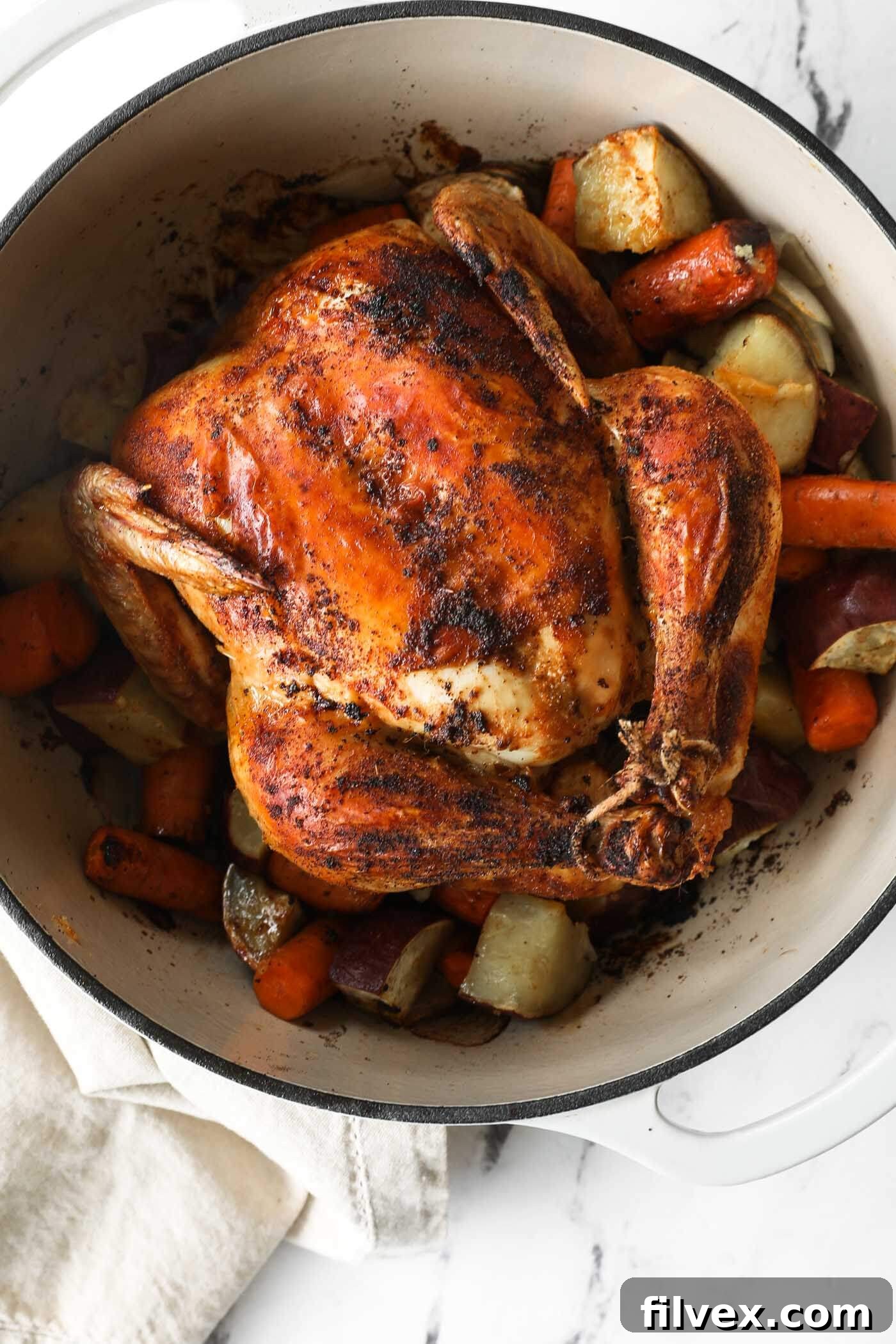 Close up overhead image of dutch oven filled with cooked veggies and a whole chicken.