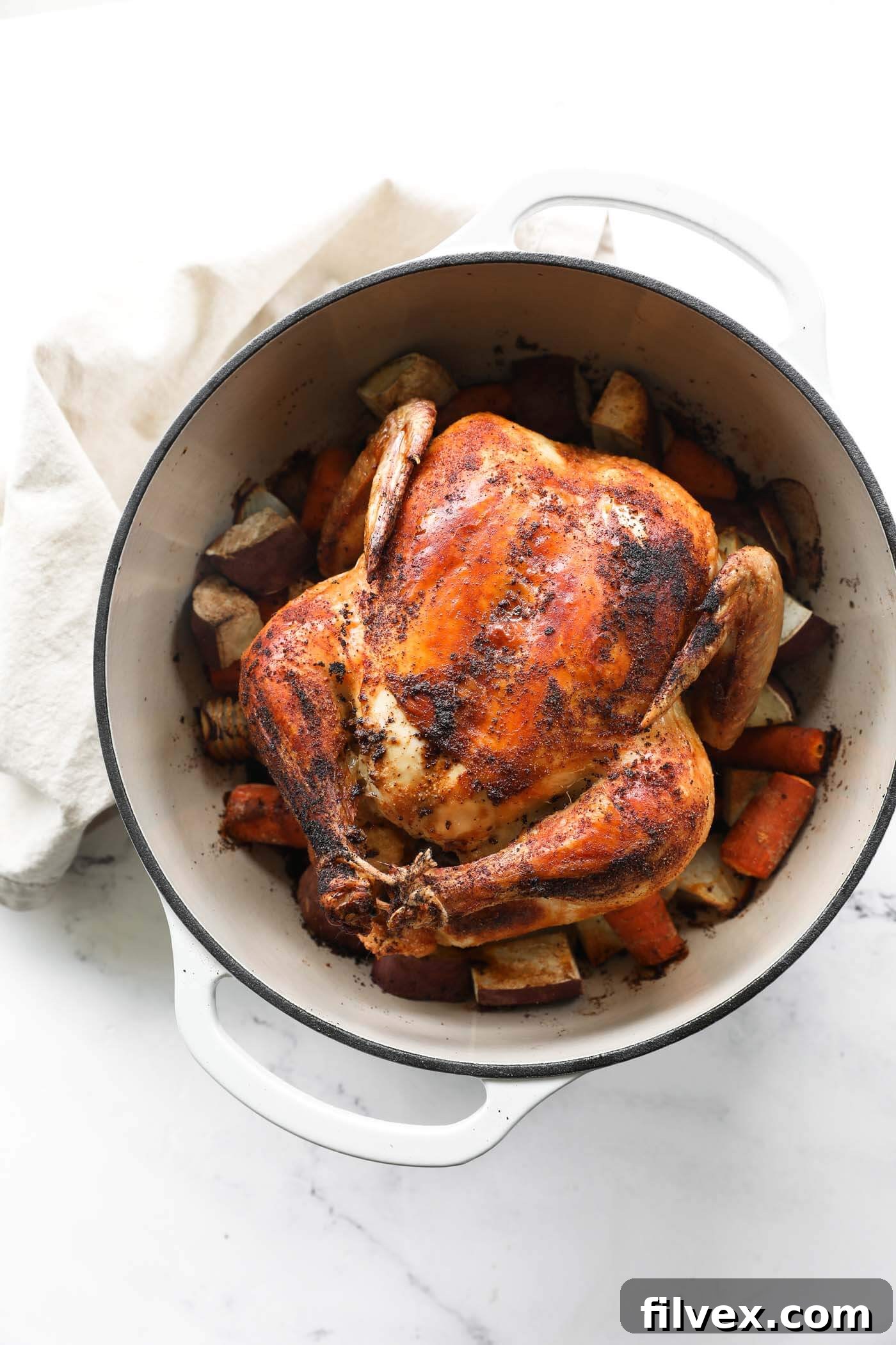 Overhead image of dutch oven filled with cooked veggies and a whole chicken.