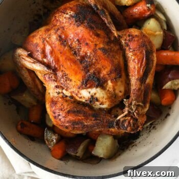 Close up overhead image of dutch oven filled with cooked veggies and a whole chicken.