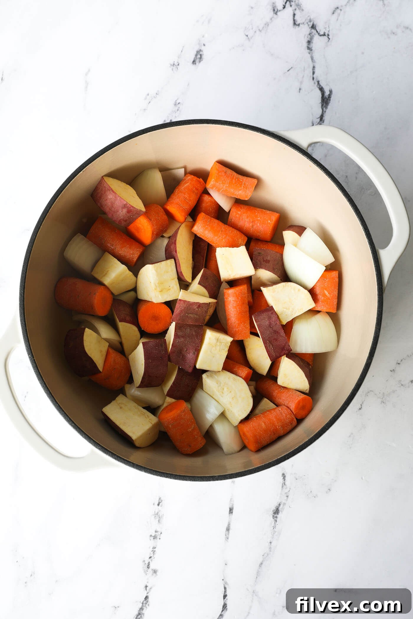 Overhead image of raw veggies - chopped potato, onion and carrots - in a dutch oven before cooking.