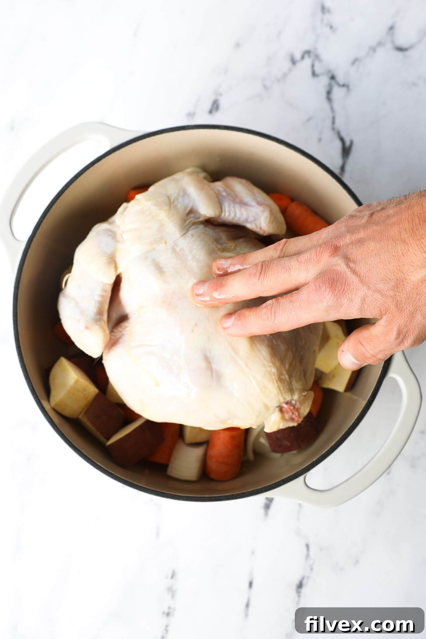 Overhead image of chicken in a dutch oven with hands rubbing olive oil on the chicken.