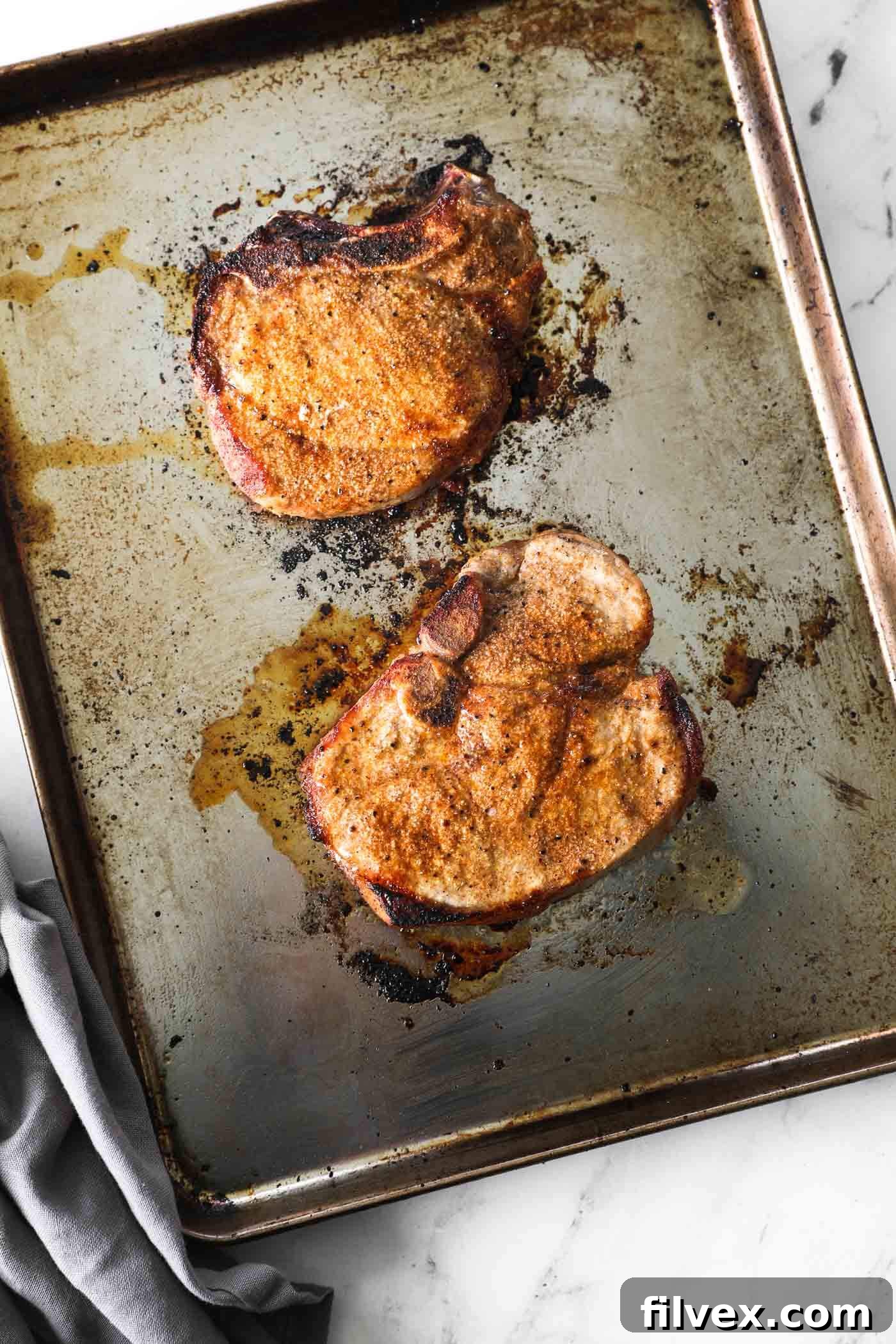Perfectly broiled pork chops with a golden-brown crust, garnished with fresh herbs and ready to be served on a sheet pan.