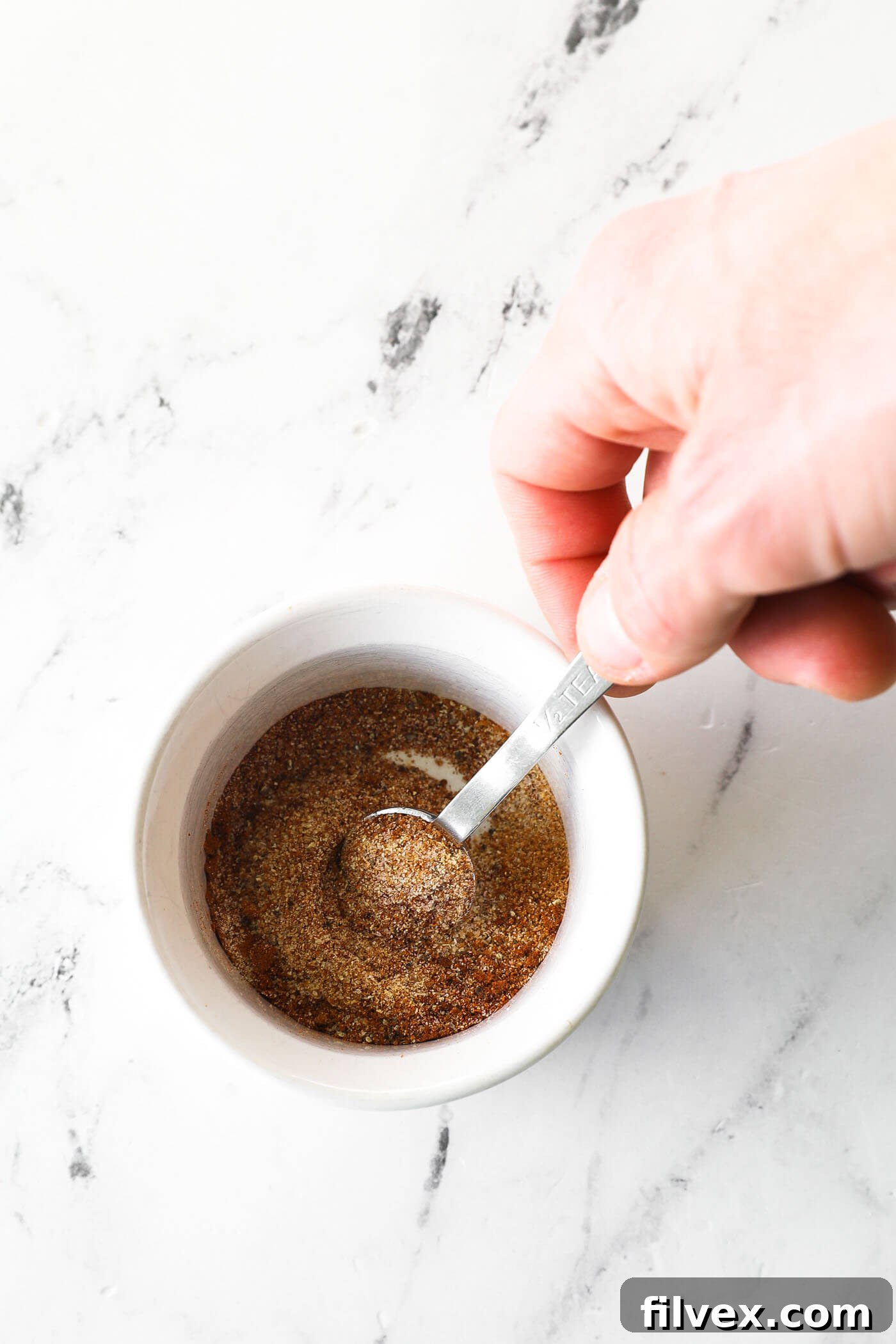 Close-up of a small bowl containing a vibrant, freshly mixed pork chop seasoning blend.