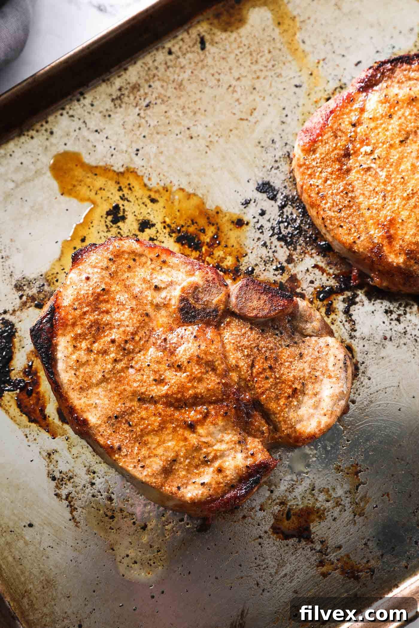A pair of perfectly cooked, juicy broiled pork chops, sliced and plated, garnished with fresh rosemary.