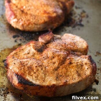 Close up angle image of broiled pork chops on a sheet pan, showing a perfect sear and inviting golden brown crust.