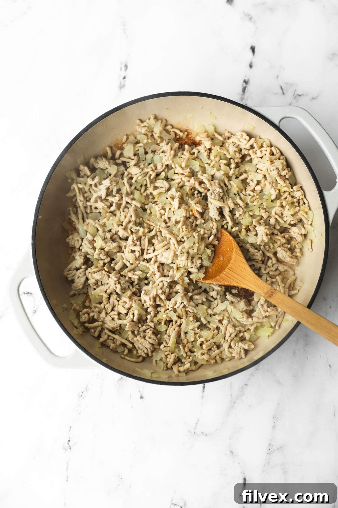 Stirring ground chicken and onion in skillet as chicken cooks until browned.