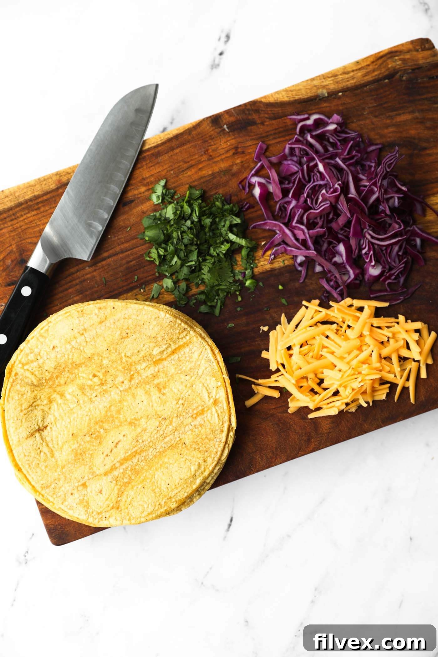 Overhead image of taco fixings on a cutting board - corn tortillas, grated cheese, chopped cabbage and cilantro.