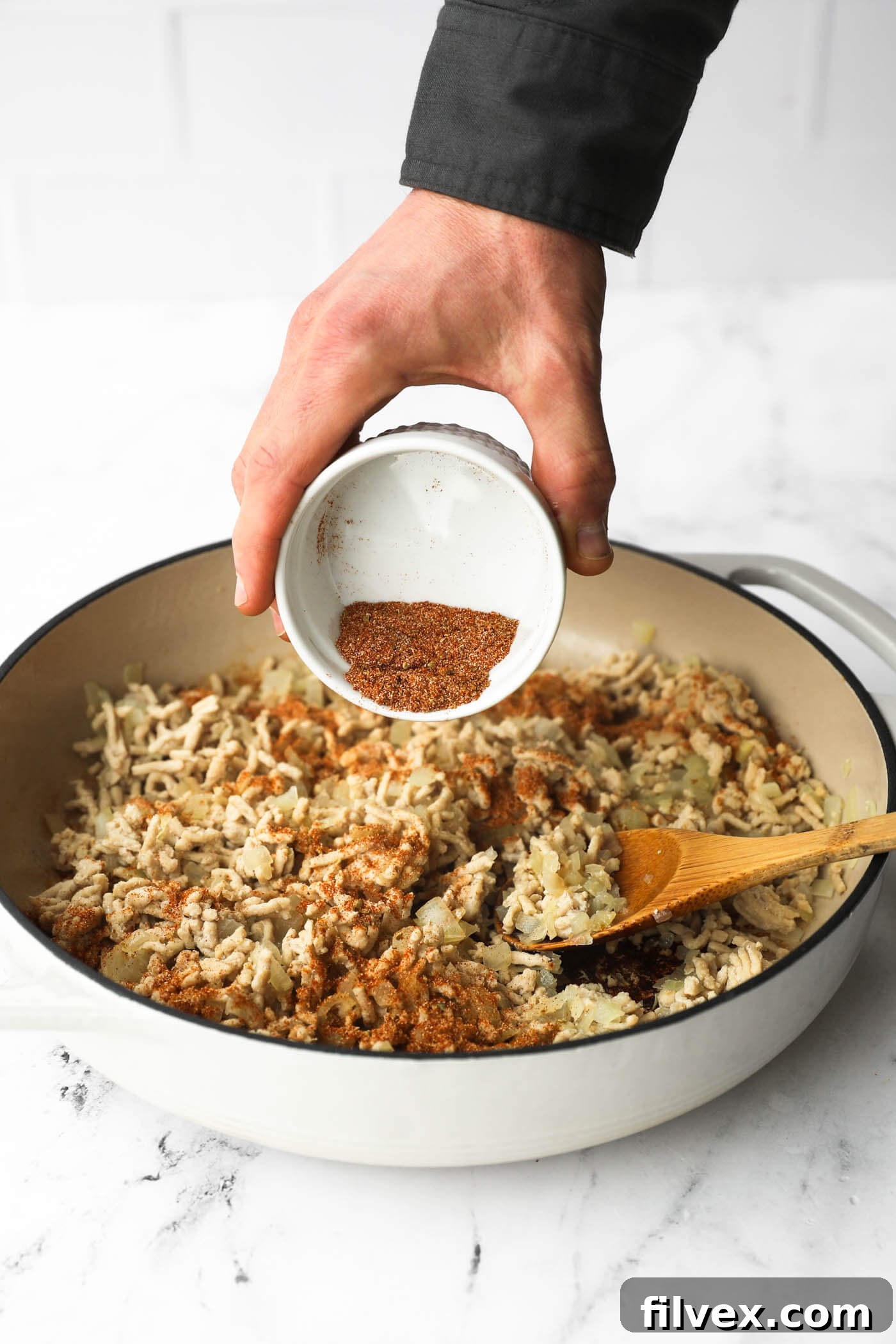 Pouring seasoning mixture into the skillet with the chicken and onion.