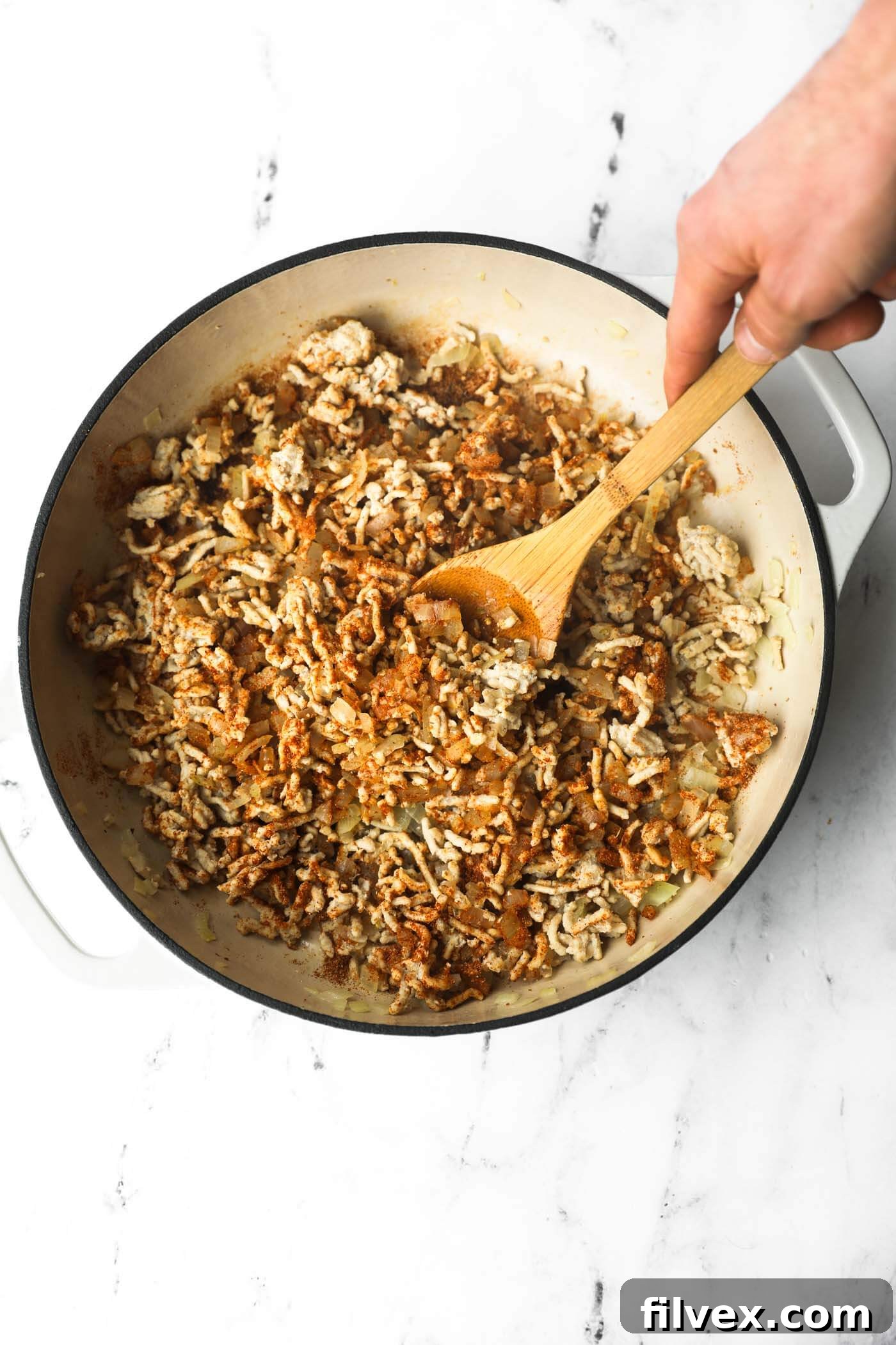 Stirring seasoning into the chicken mixture in the skillet.