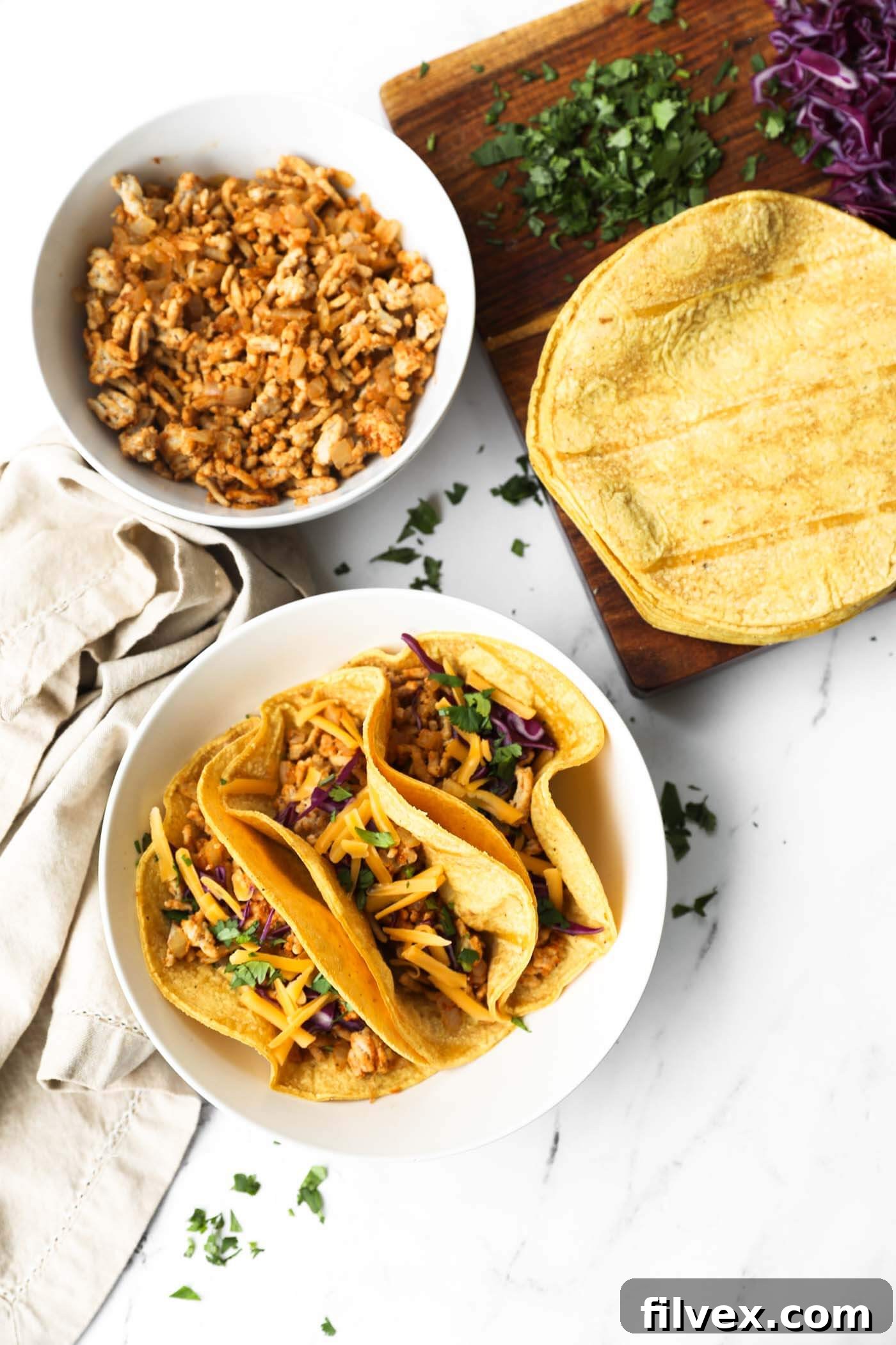 Overhead image of three tacos in a bowl with taco fixings surrounding the bowl - extra tortillas, a bowl of ground chicken mixture.
