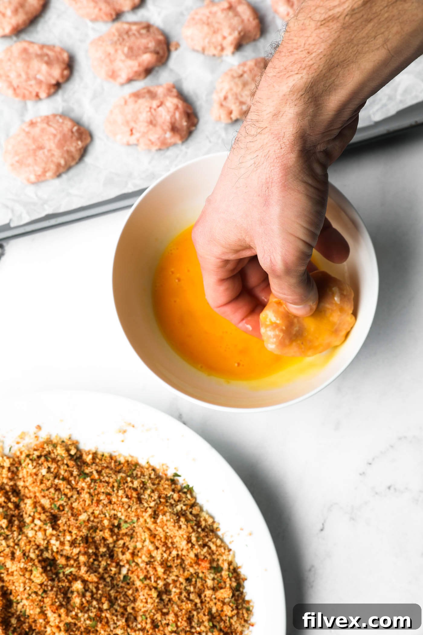 Dipping a chicken nugget into whisked egg to coat it