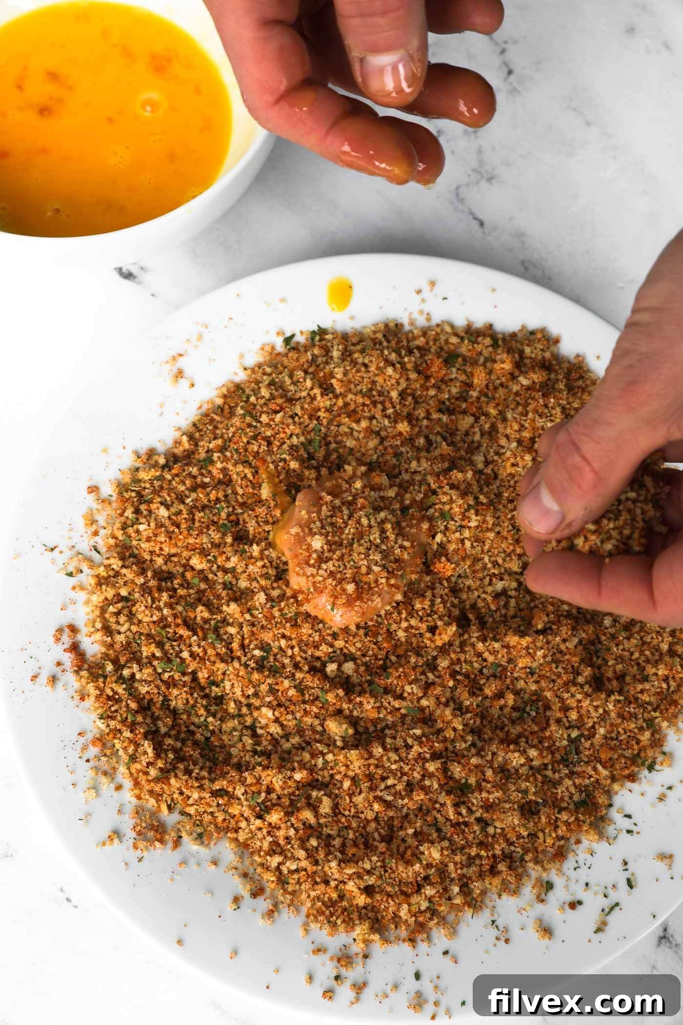 Dredging an egg-coated chicken nugget in breadcrumb mixture