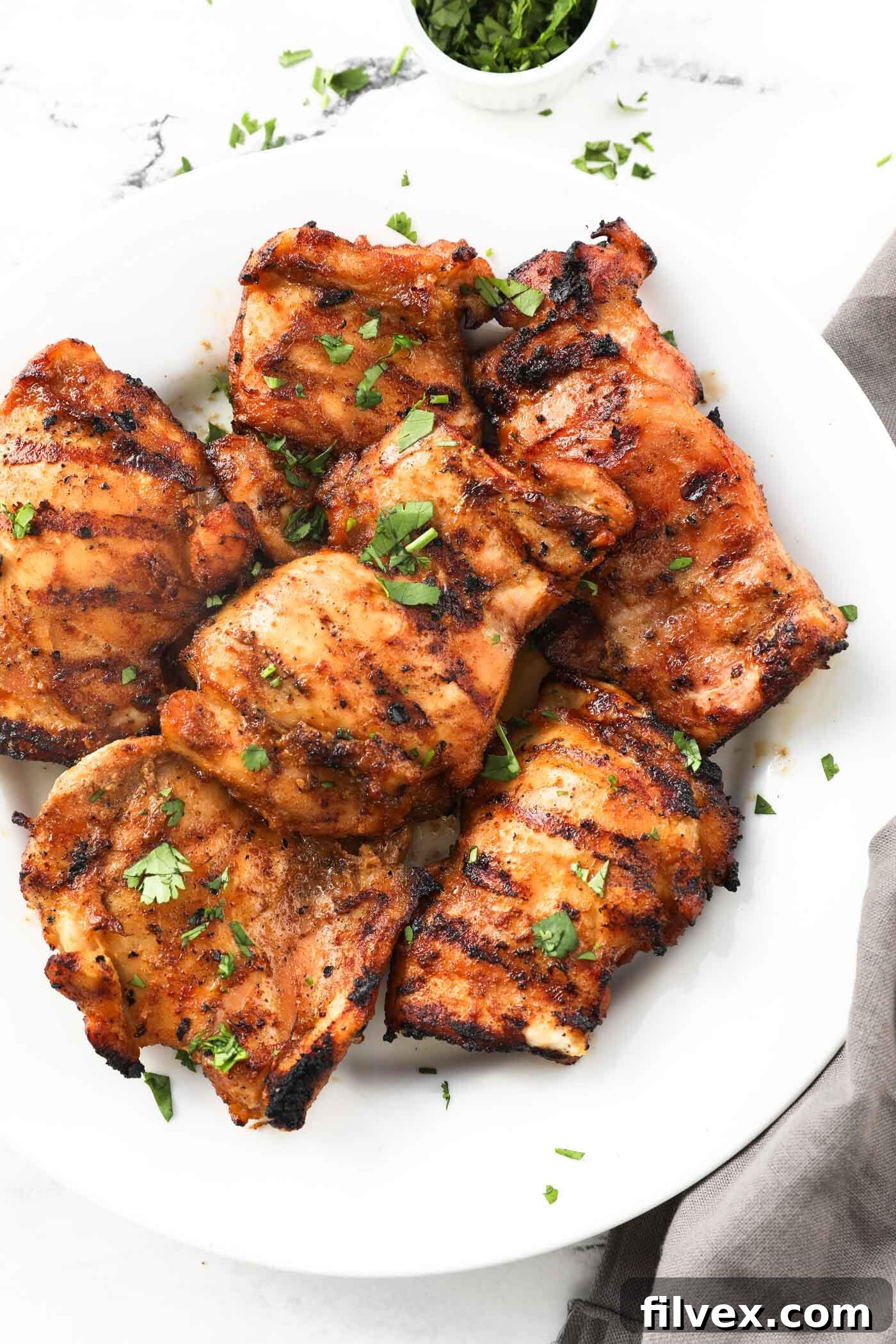 Overhead image of a plate of grilled chicken thighs with chopped cilantro on top. A perfectly cooked, golden-brown chicken thigh resting on a plate, garnished with fresh herbs, showcasing its delicious char and moist interior, ready to be enjoyed.