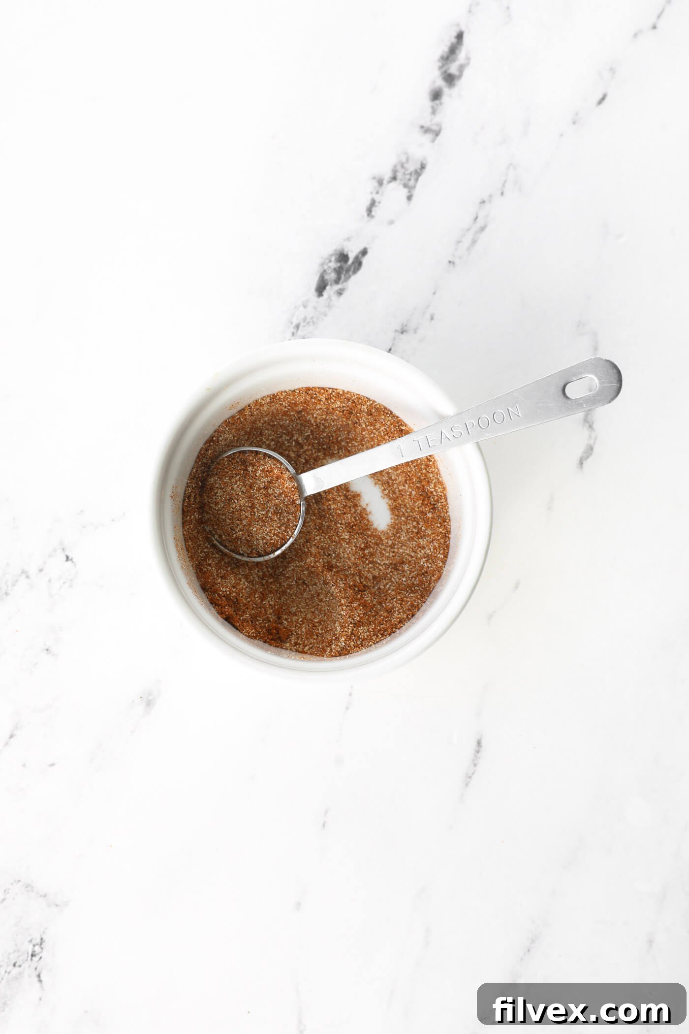 Ramekin of seasonings mixed up with a teaspoon. A small bowl containing a vibrant mixture of aromatic spices, perfectly blended and ready to be sprinkled on the chicken for maximum flavor.