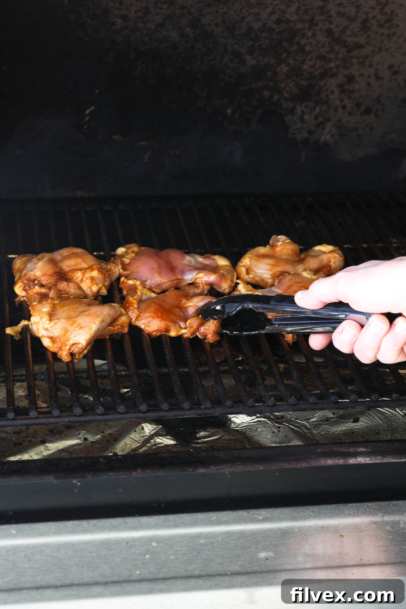 Putting seasoned chicken thighs onto the grill with tongs. Perfectly seasoned chicken thighs being carefully placed onto hot, clean grill grates, ready to develop their delicious char.