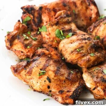 Angled image of a plate of grilled chicken thighs with chopped cilantro sprinkled on top. A plate of perfectly grilled, juicy chicken thighs, garnished with fresh cilantro, invitingly ready to be served.