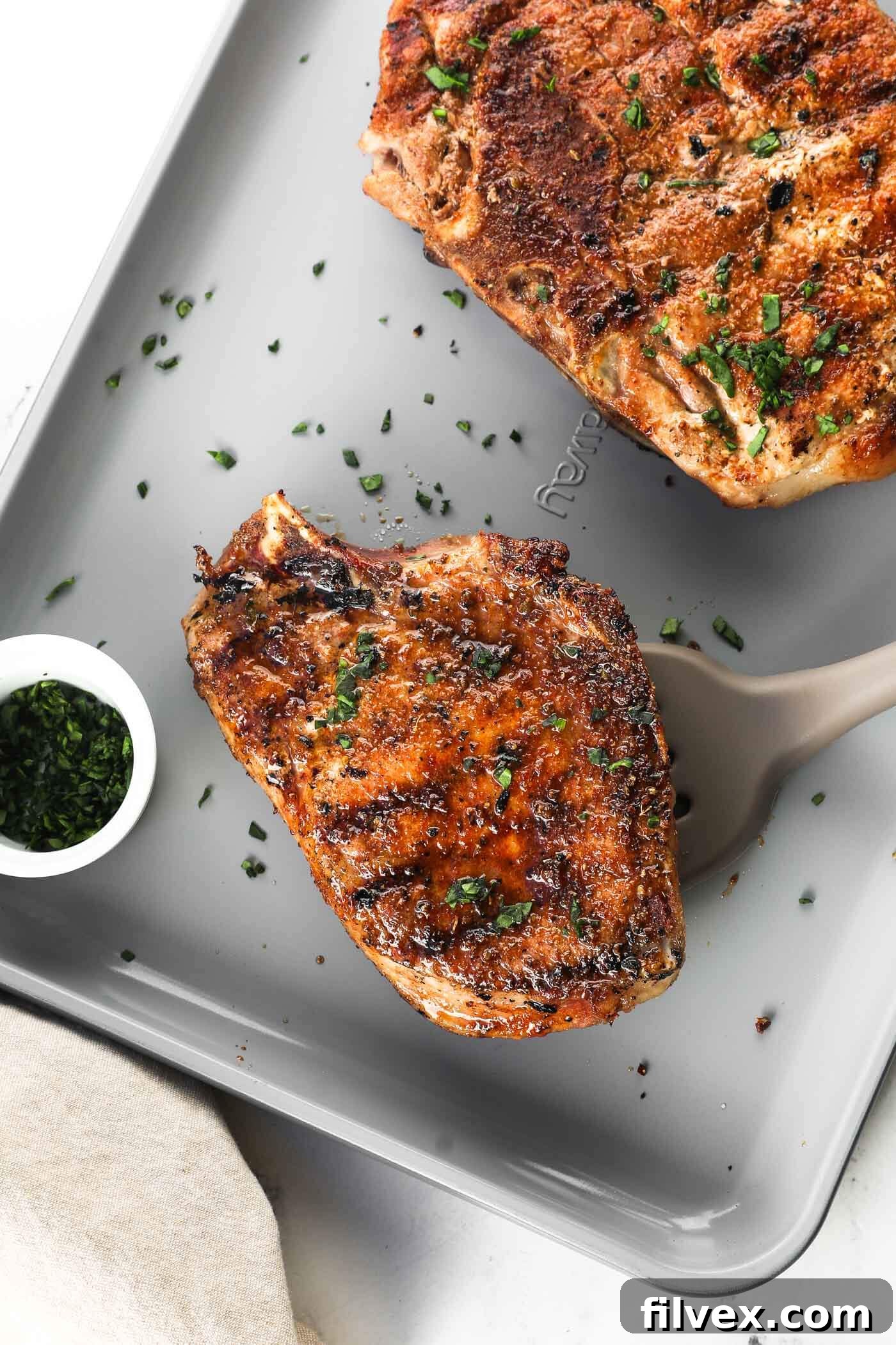 Two perfectly grilled bone-in pork chops on a rustic wooden board, garnished with fresh herbs, showcasing their golden-brown crust and tender interior.