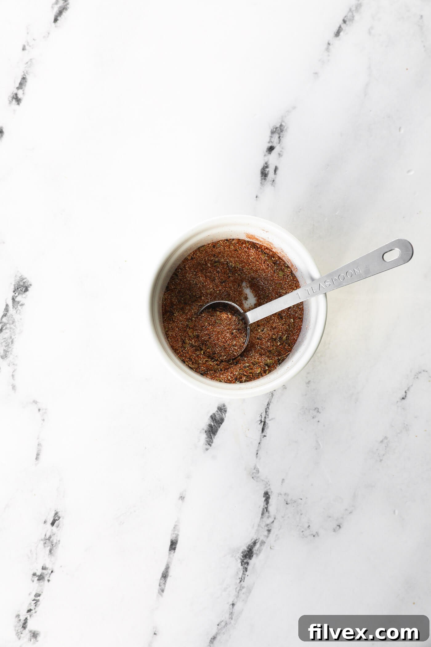 A small bowl filled with a blend of vibrant spices for the pork chop seasoning, ready to be mixed.