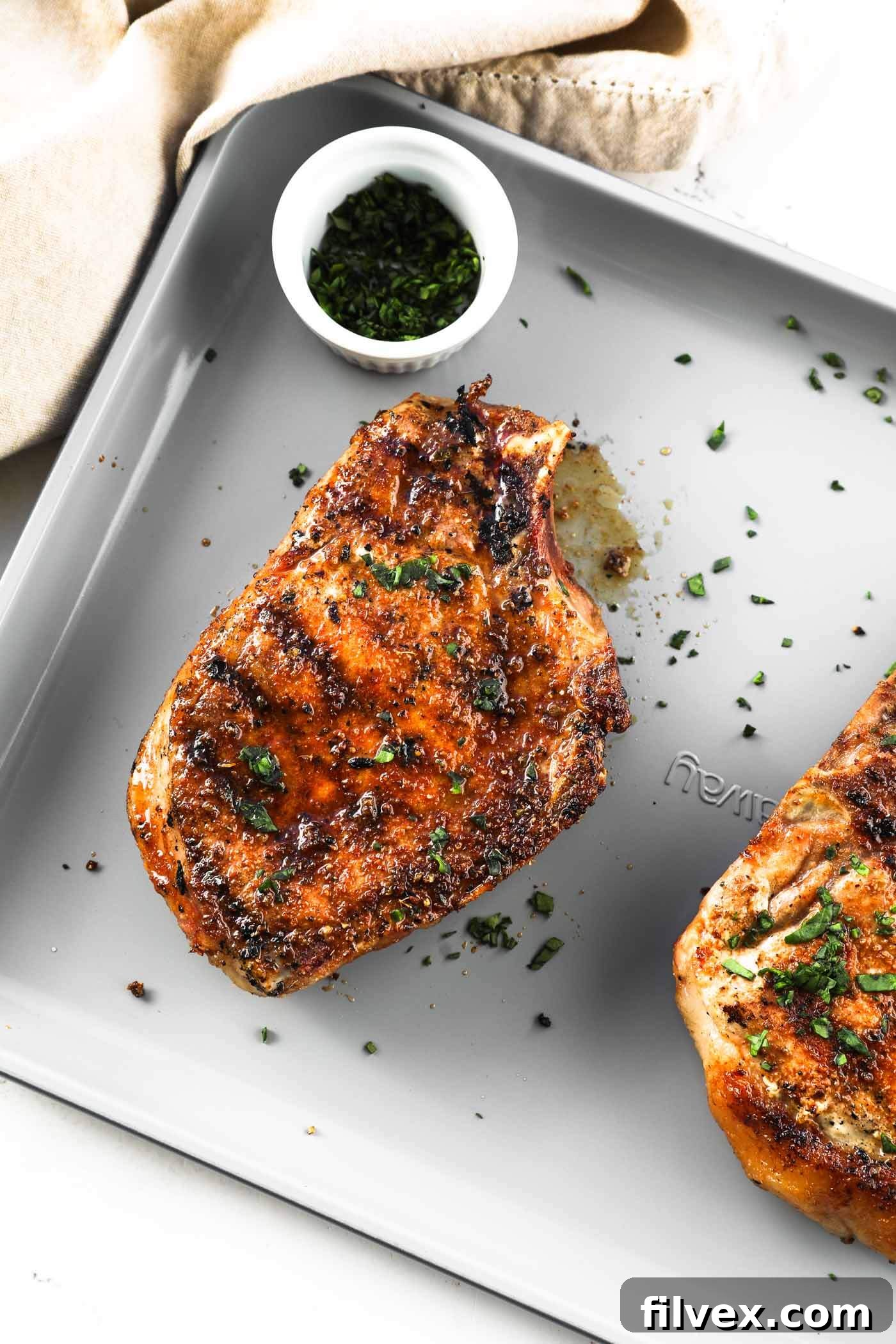 A stack of three perfectly grilled bone-in pork chops on a wooden cutting board, ready to be served.