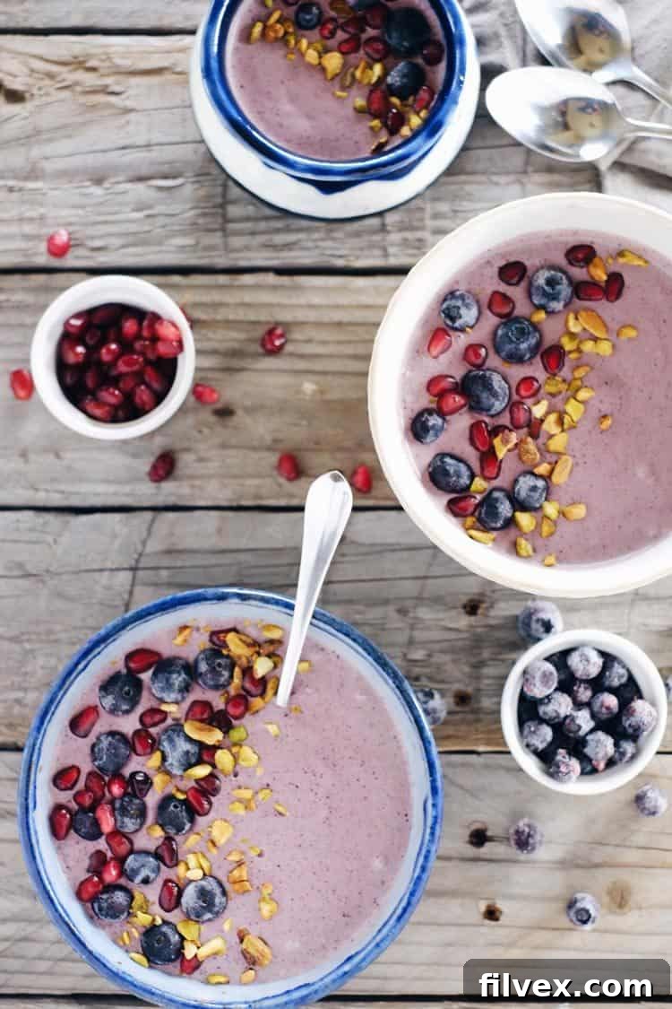 Two berry protein smoothie bowls topped with fresh blueberries, pomegranate seeds, and chopped nuts.