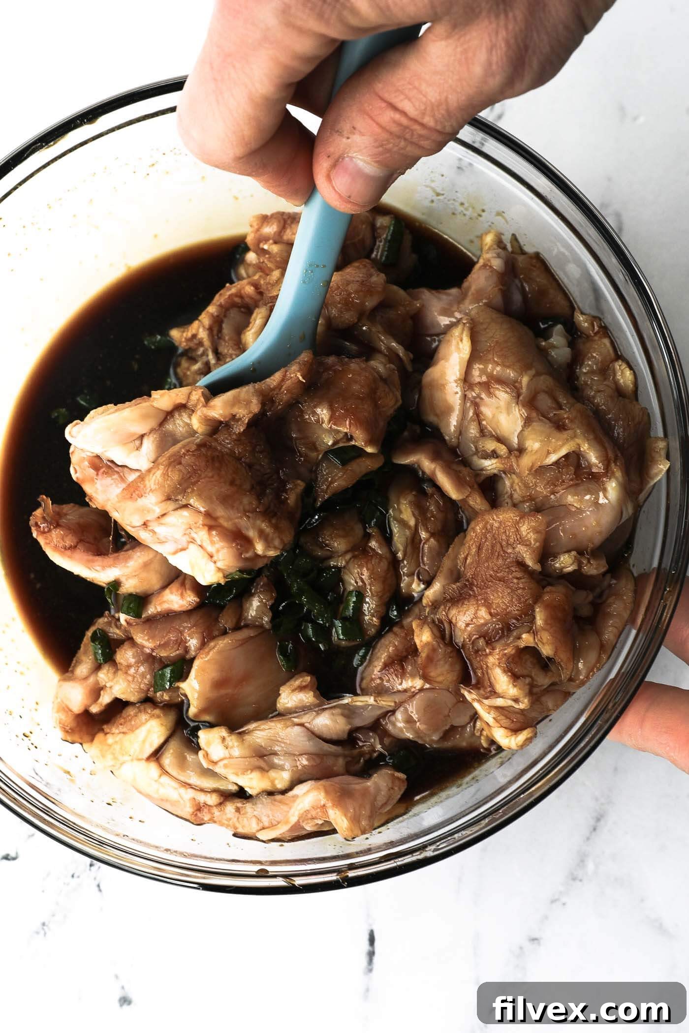 Raw chicken being stirred in a bowl, thoroughly coated with homemade teriyaki marinade, ready for cooking.