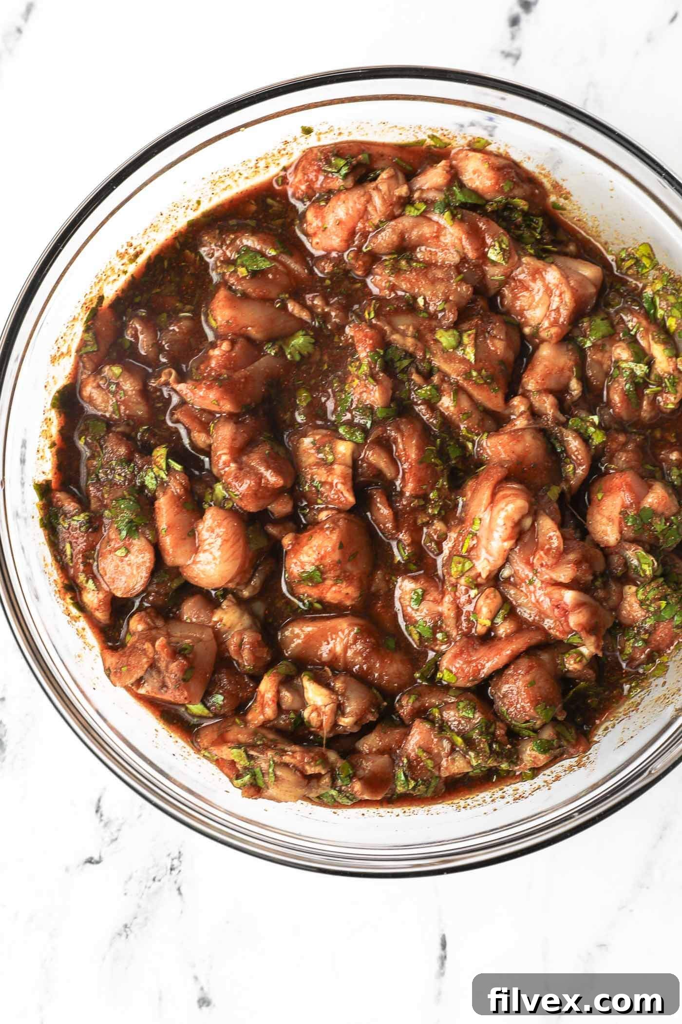 Close up overhead image of a glass bowl full over cut up chicken with a fajita marinade coating everything. 