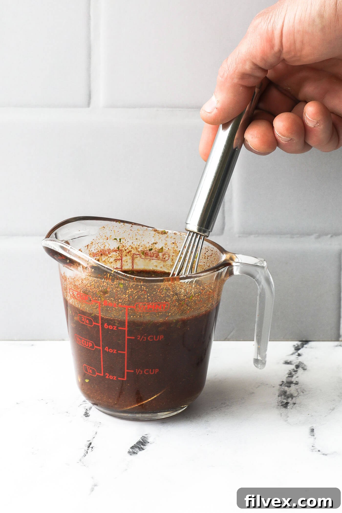 Using a whisk to stir fajita marinade ingredients together in a glass measuring cup.