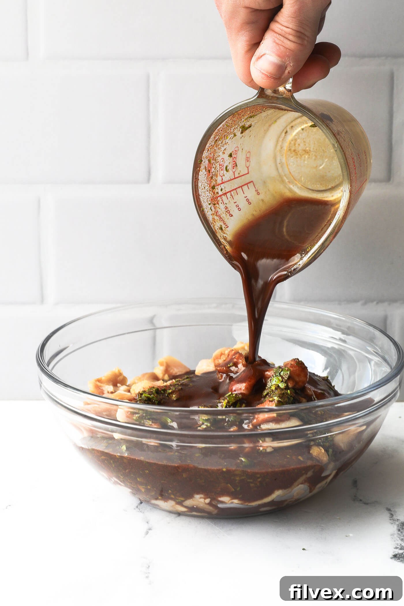 Pouring fajita marinade over a bowl of sliced raw chicken.