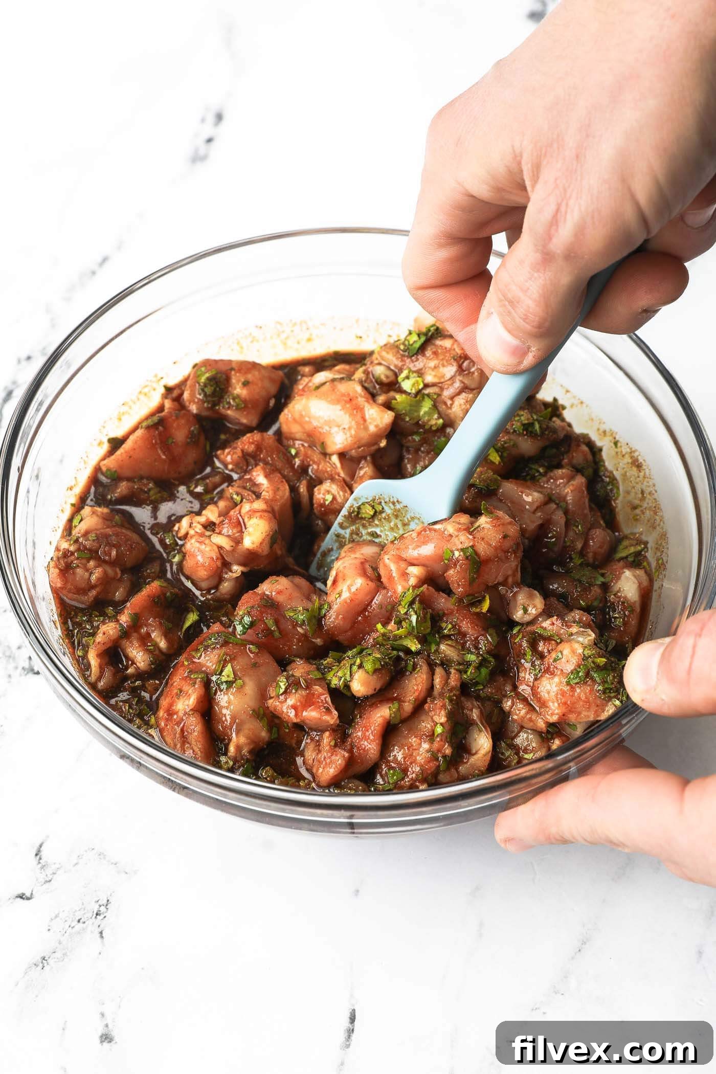 Using a spatula to combine fajita marinade with raw chicken in a glass bowl.
