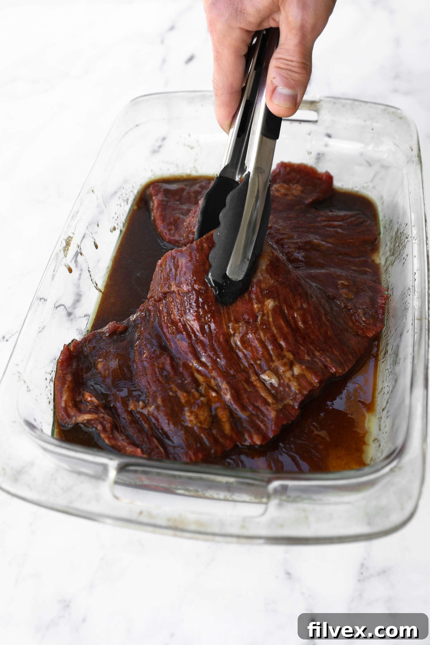 Pouring the balsamic marinade over raw chicken breasts in a shallow white dish, ensuring full coverage.