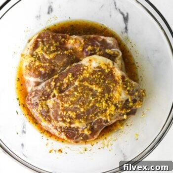 Pork chops in a bowl covered in honey mustard marinade, ready to be cooked.