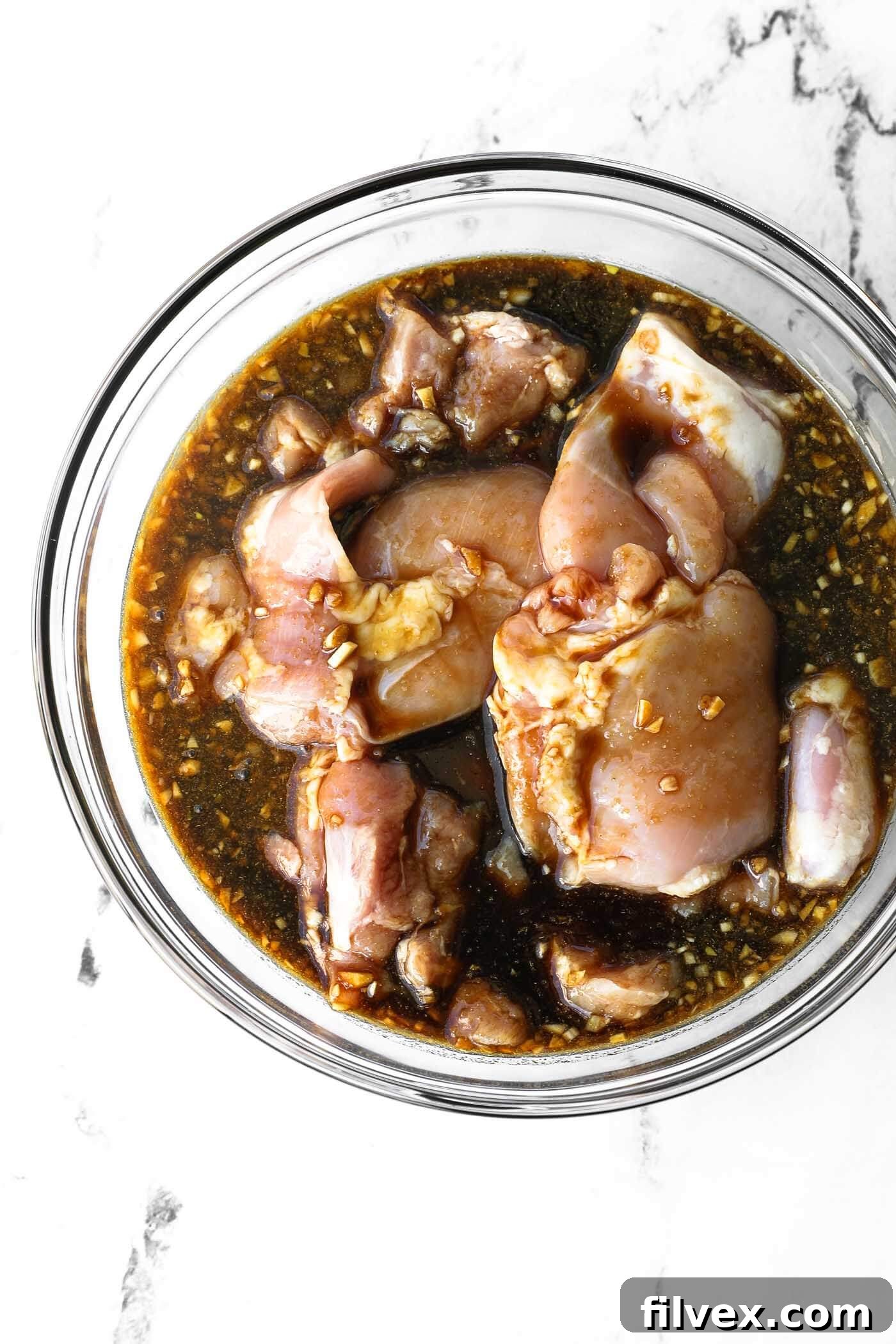 Raw chicken marinating in a bowl with honey garlic sauce.