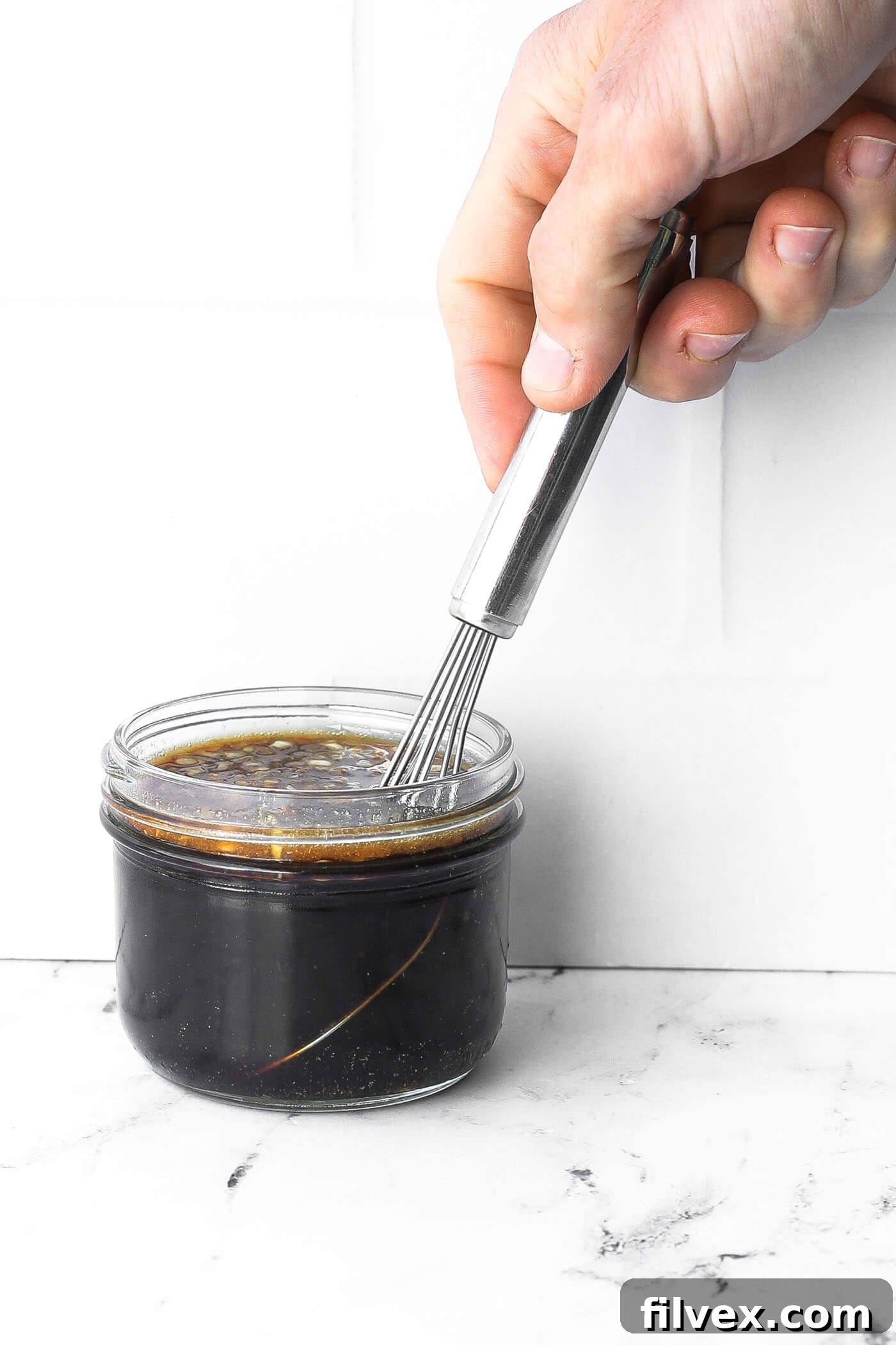 Stirring honey garlic marinade in a small jar with a whisk.