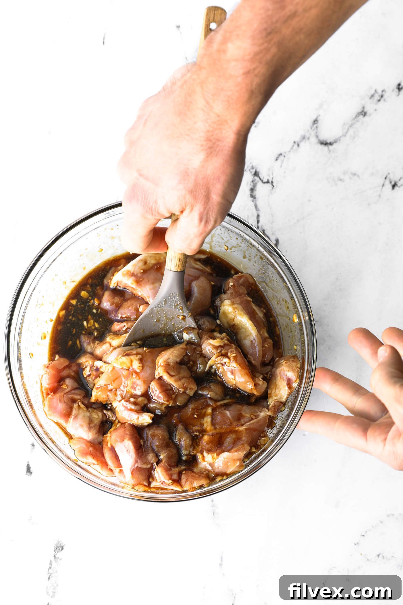 Mixing raw chicken with the honey garlic marinade in a glass bowl.