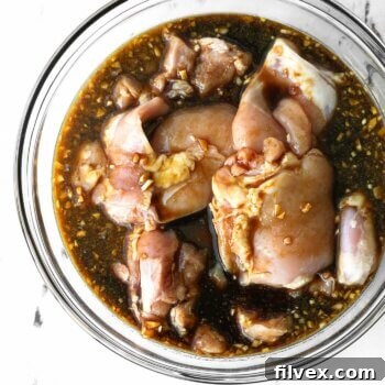 Raw chicken marinating in a bowl with honey garlic sauce.