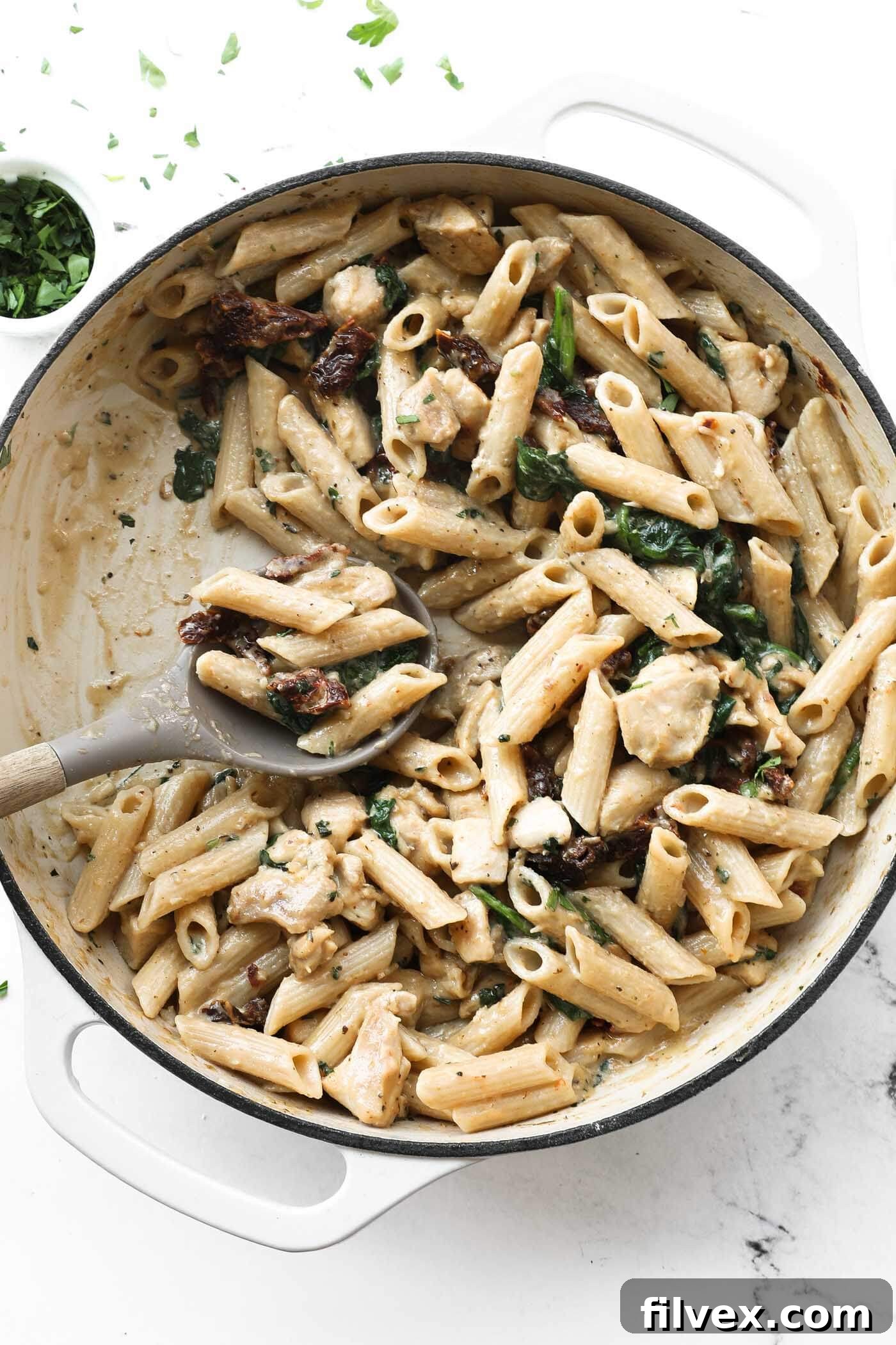 Close-up of creamy chicken pasta in a skillet, garnished with fresh basil.