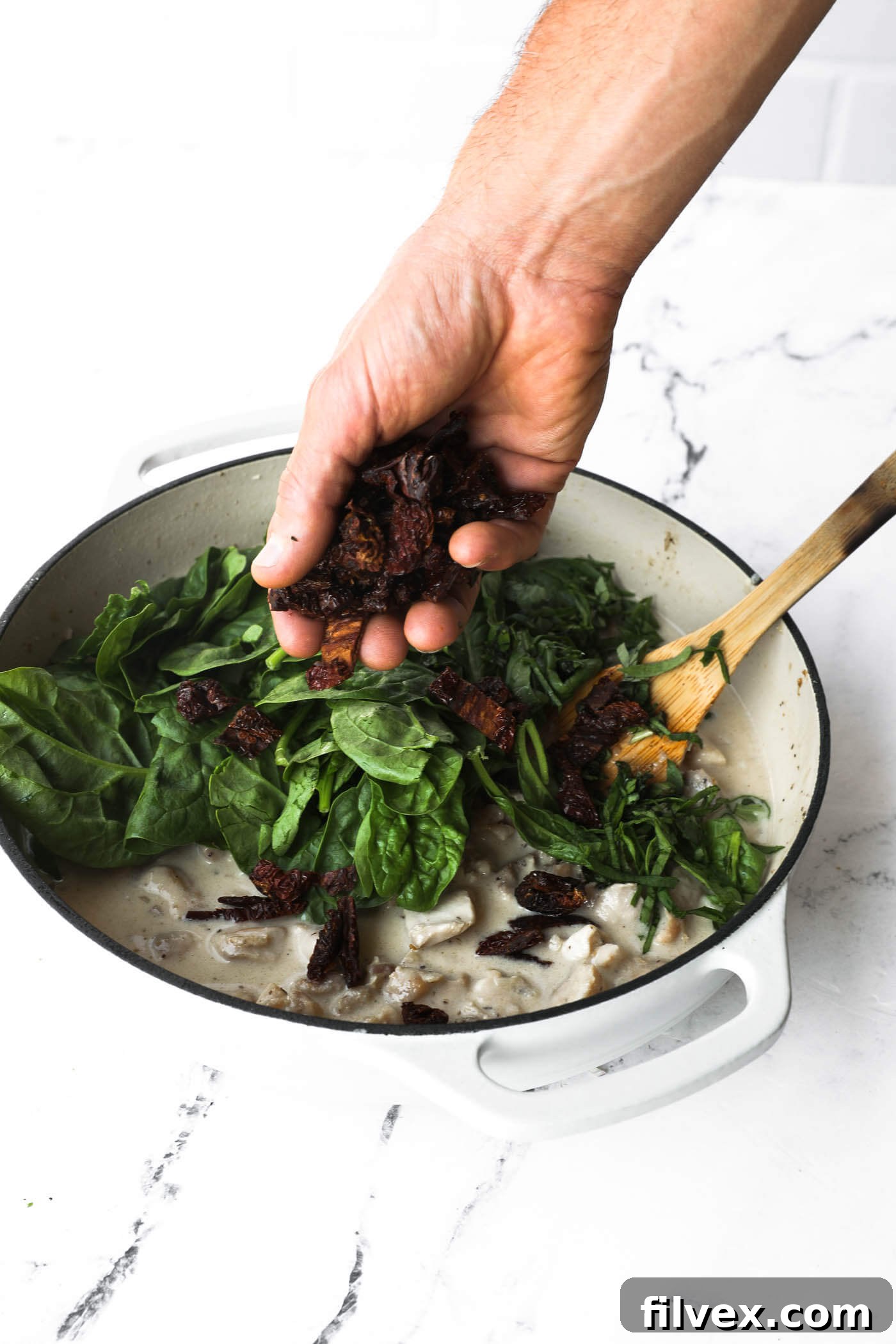 Spinach, basil, and sun-dried tomatoes added to the creamy sauce in a skillet.