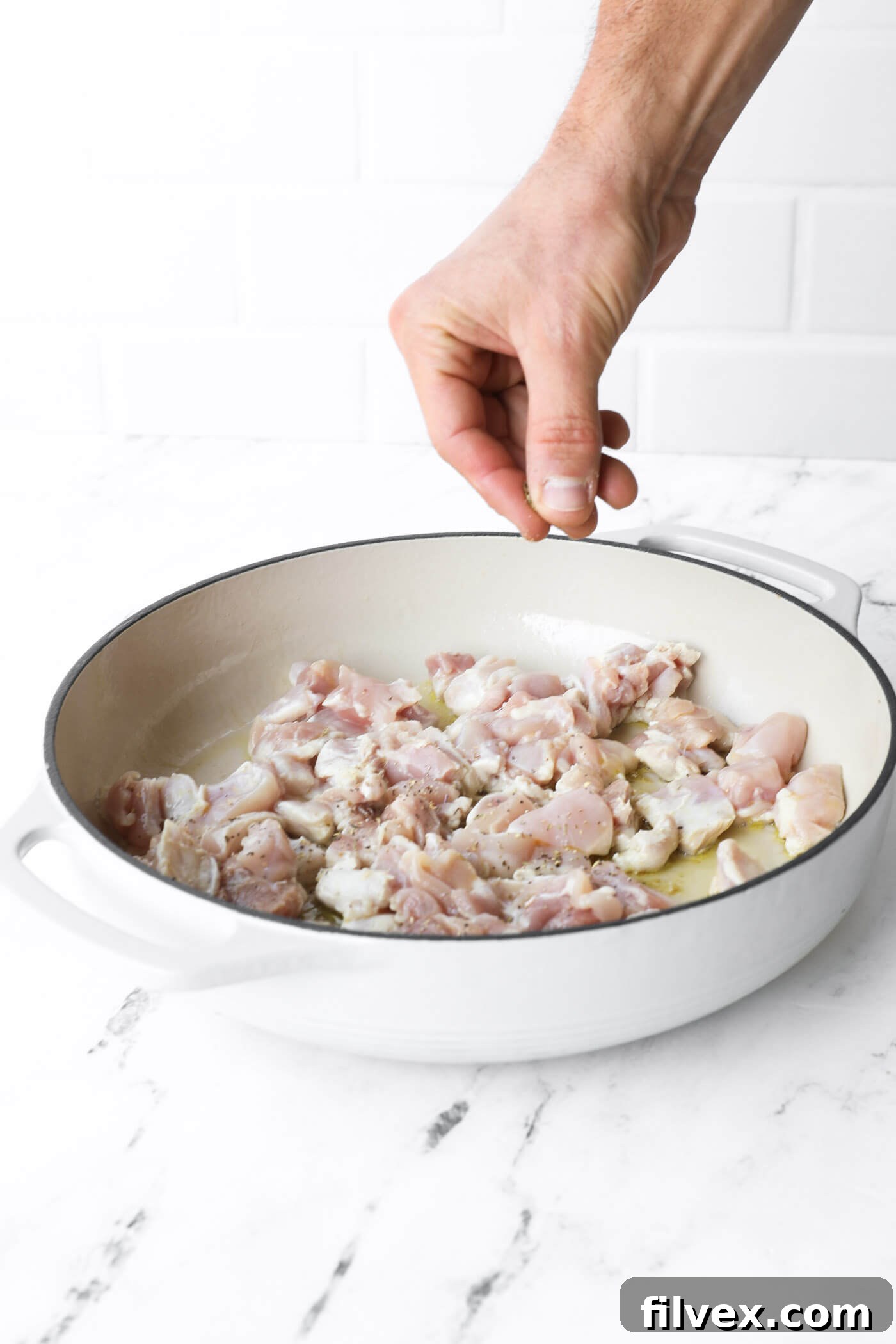 Chicken pieces sizzling in a hot skillet with seasoning.