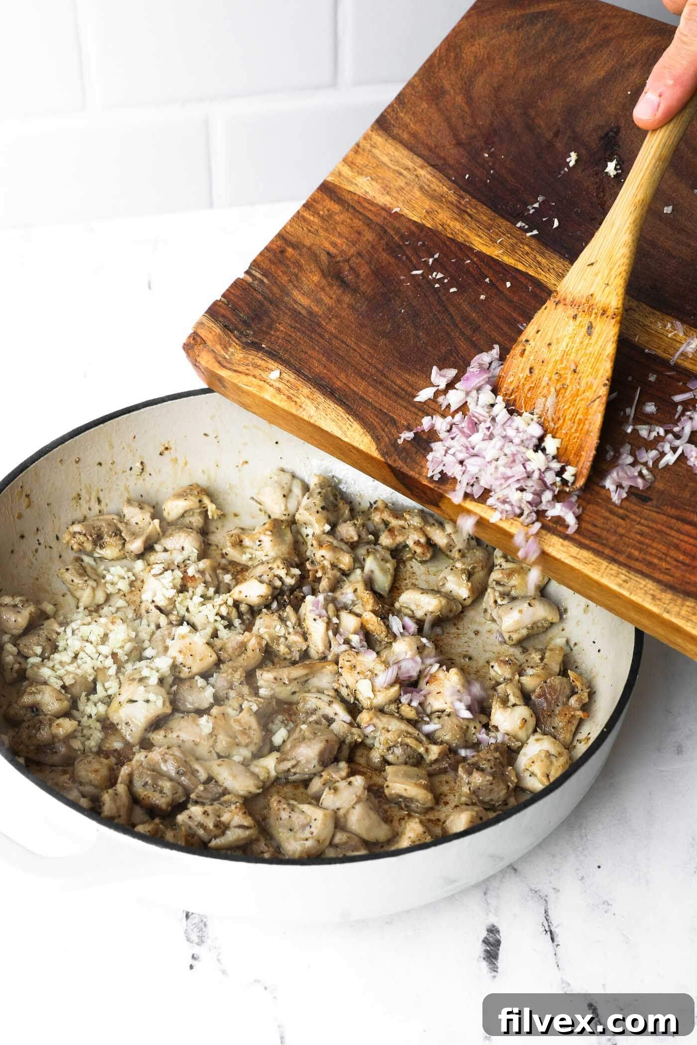 Minced garlic and diced shallots added to cooking chicken in a skillet.